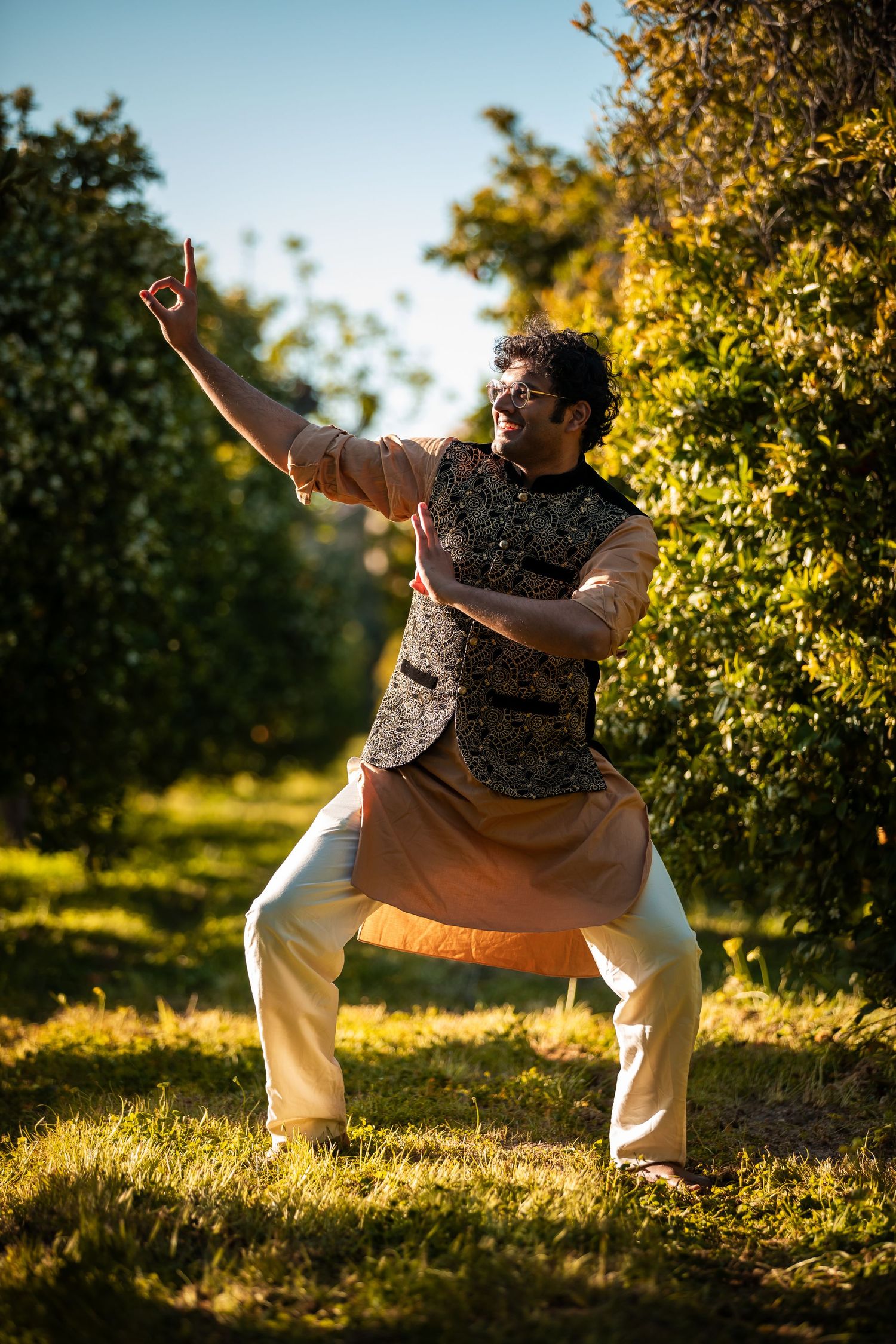 Figure performs expressive dance moves in sunlit garden setting.
