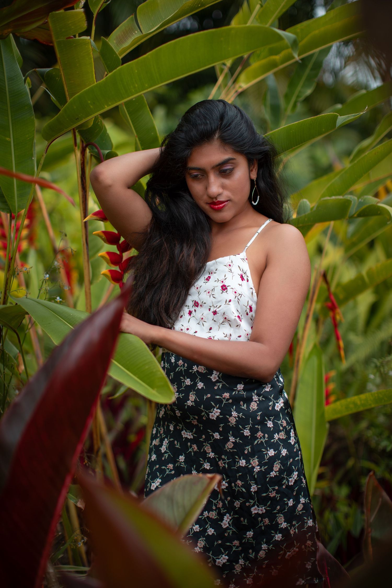 A floral summer outfit photoshoot among tropical plants with a white top and patterned skirt.