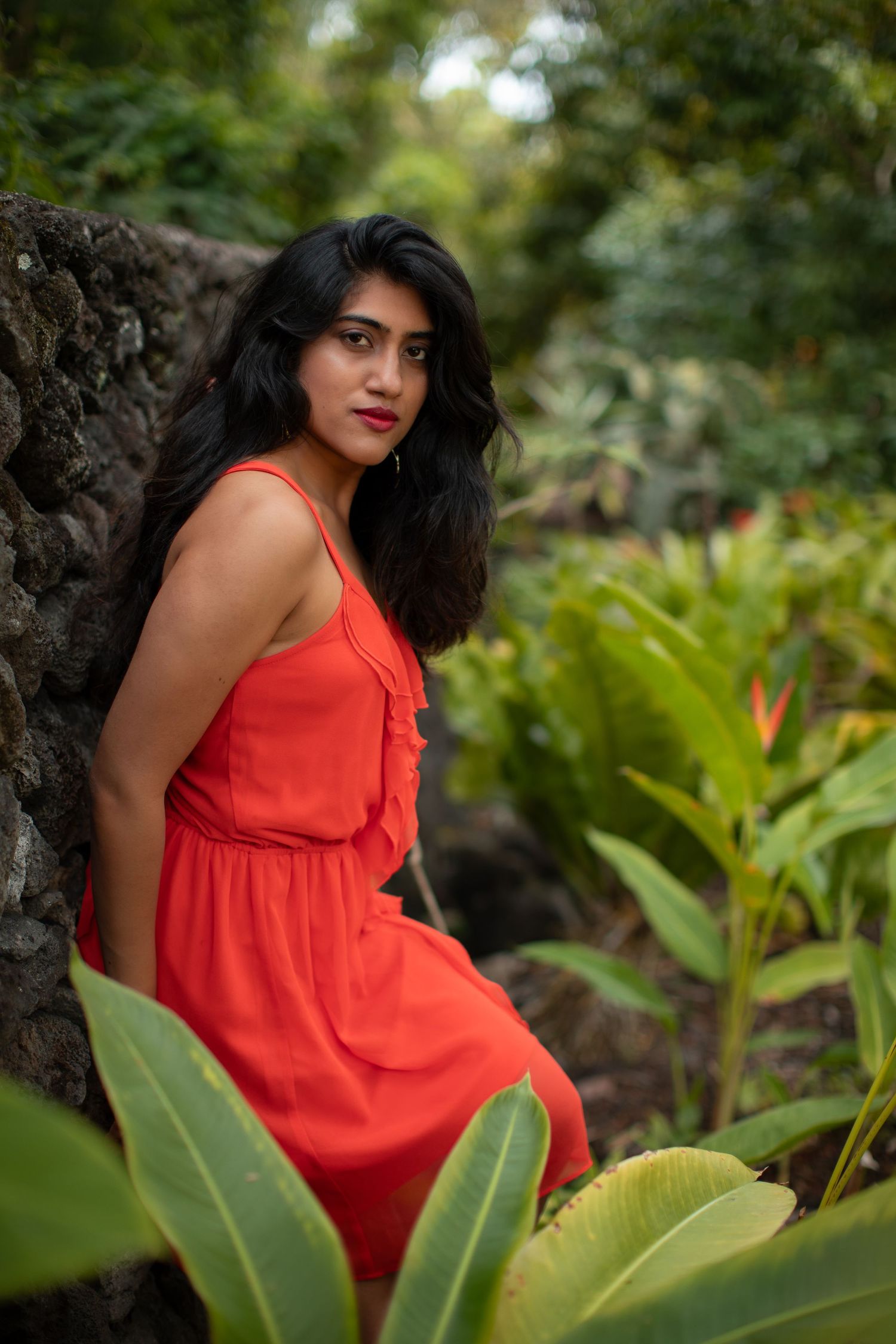 A vibrant orange dress stands out against lush tropical foliage in an outdoor portrait session.