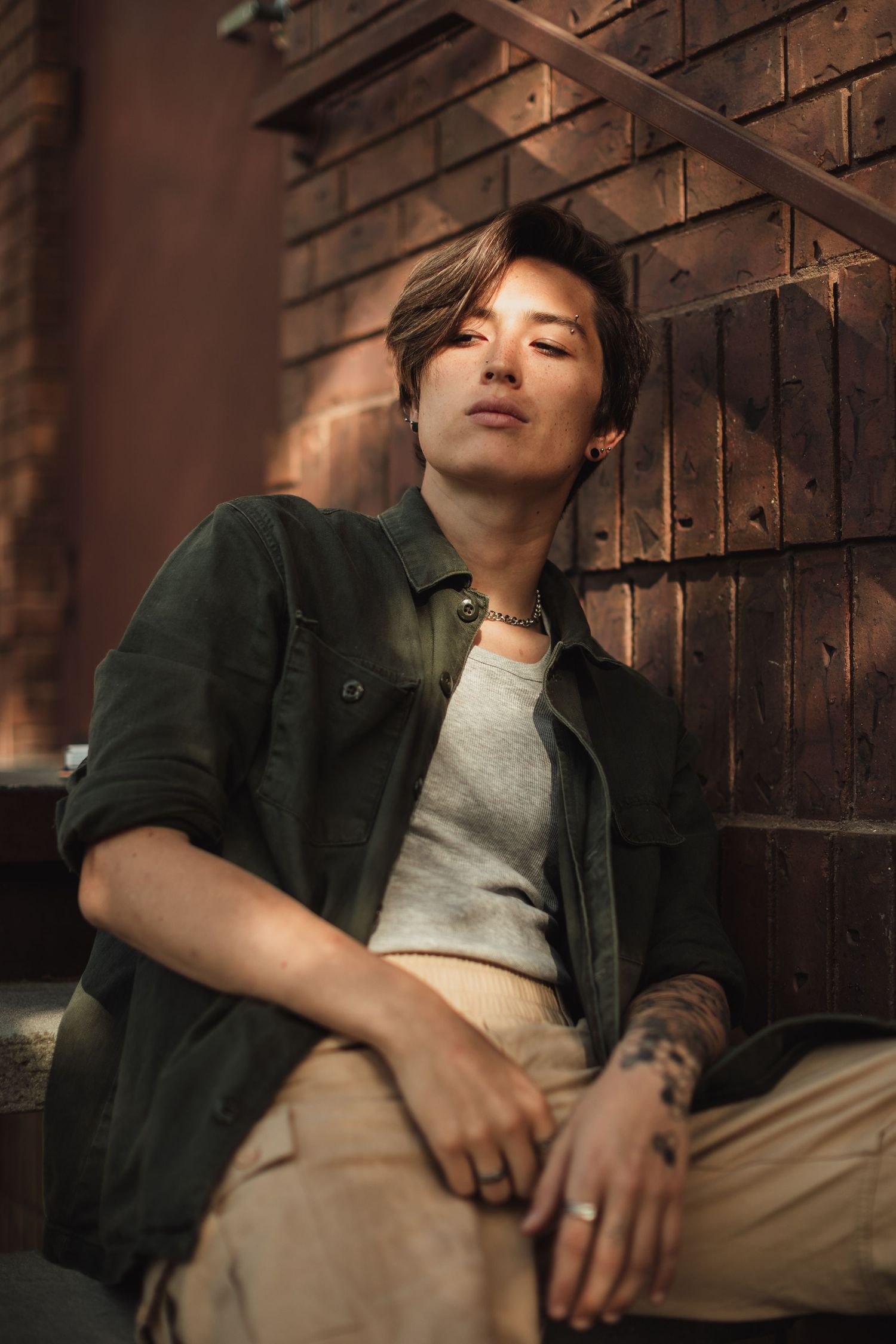 Casual pose against rustic wooden wall wearing green jacket and light colored pants.