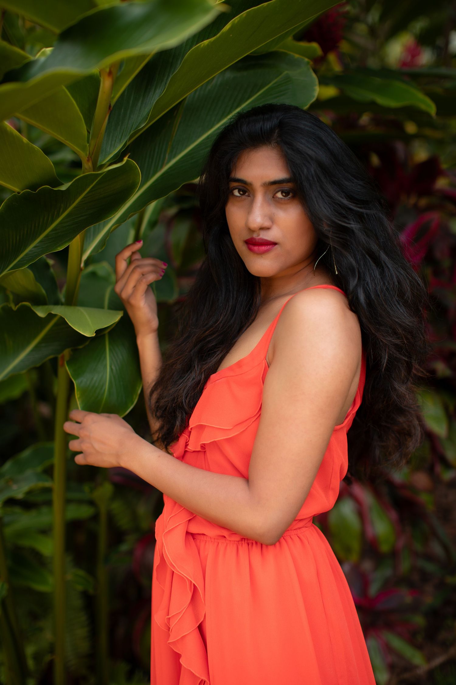 Artistic portrait with flowing orange dress against large green tropical leaves.