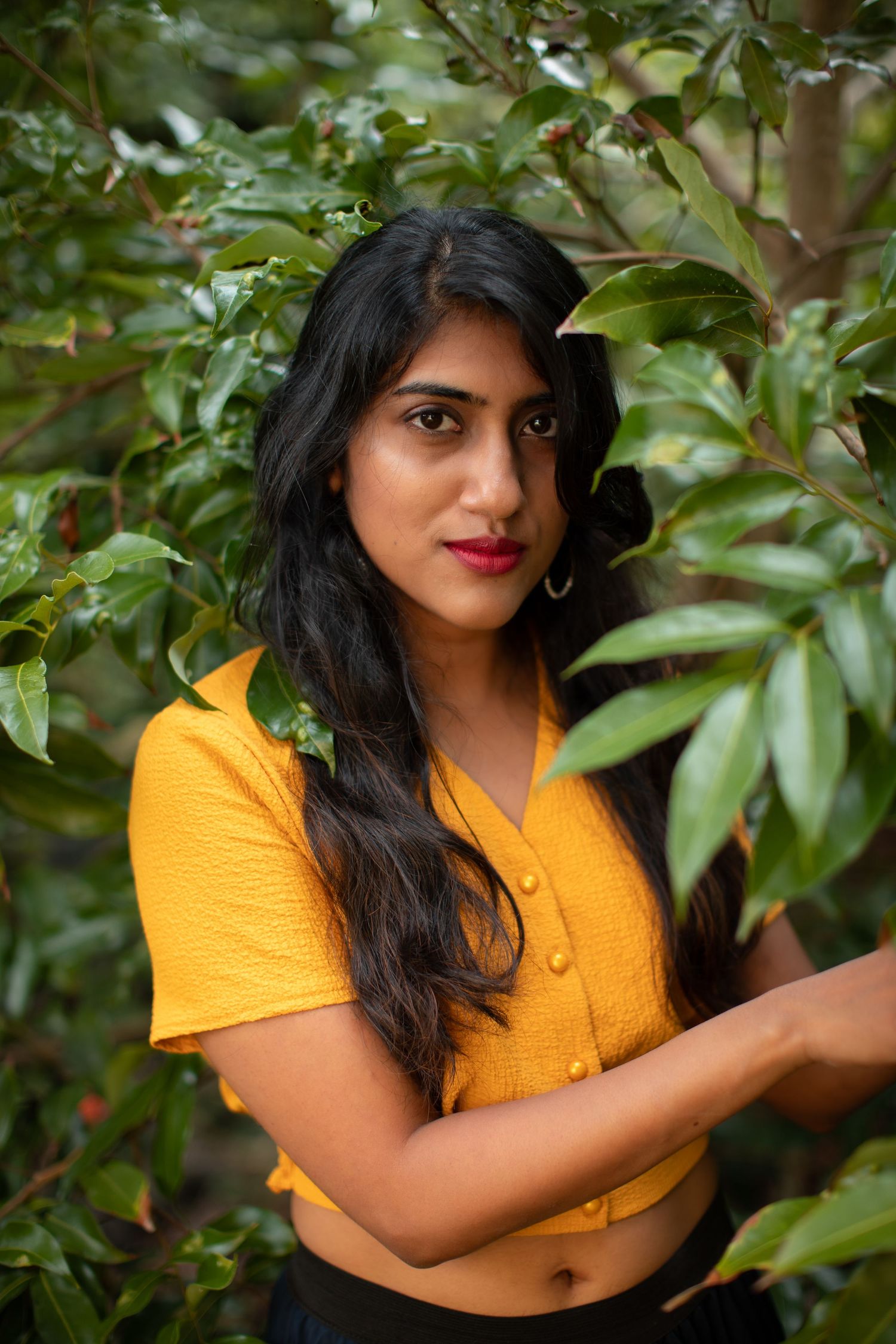 Casual outdoor portrait in yellow top surrounded by green garden foliage.
