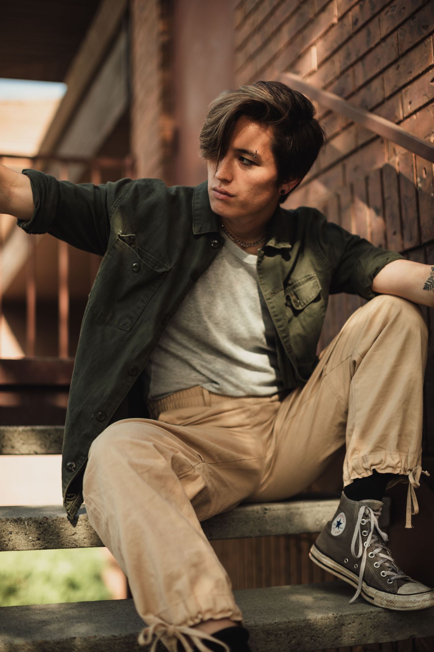 Relaxed pose on wooden steps showing casual streetwear and sneakers.