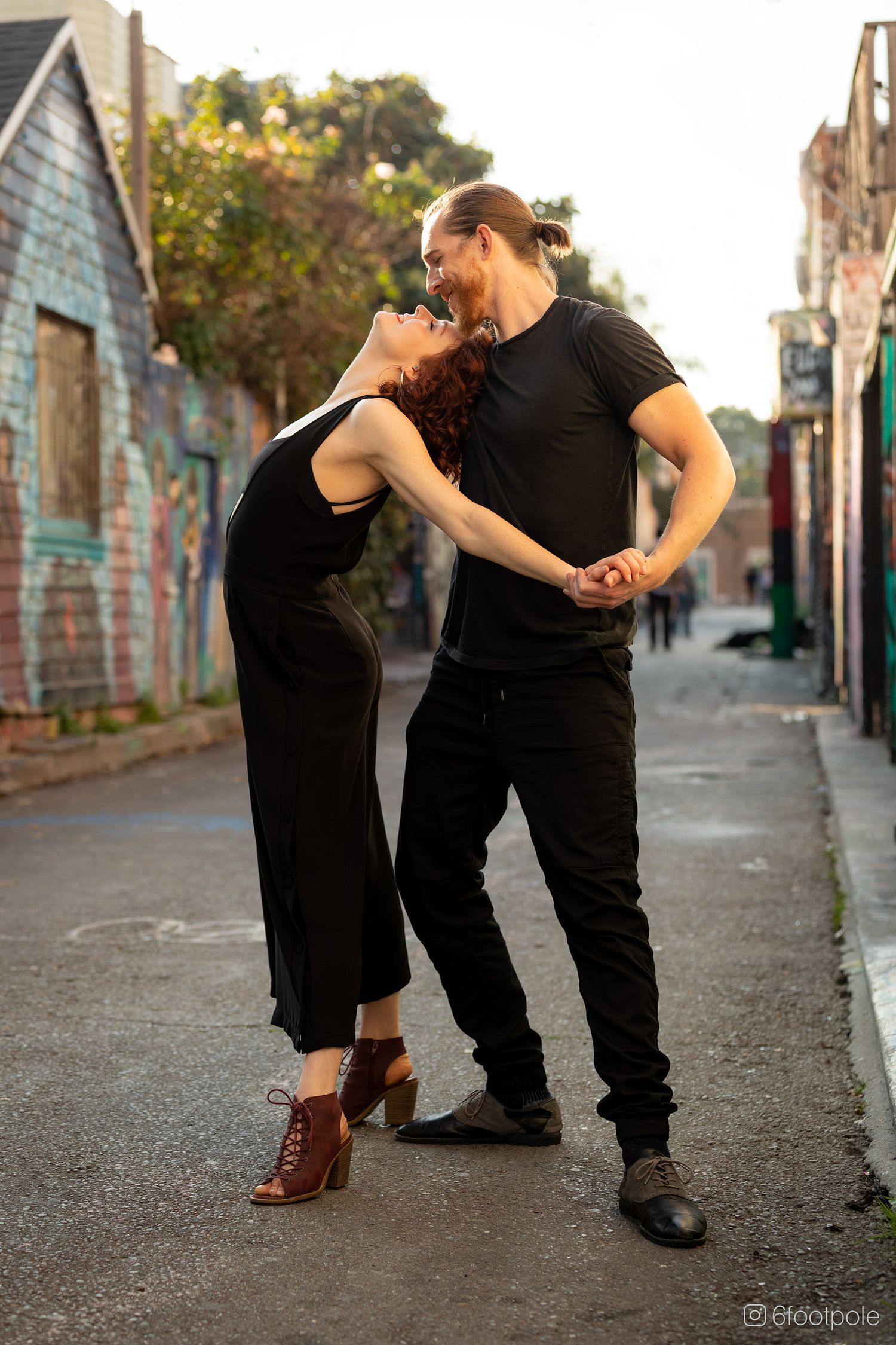 A couple in black outfits dancing together in an urban alleyway with brick walls and dramatic lighting.