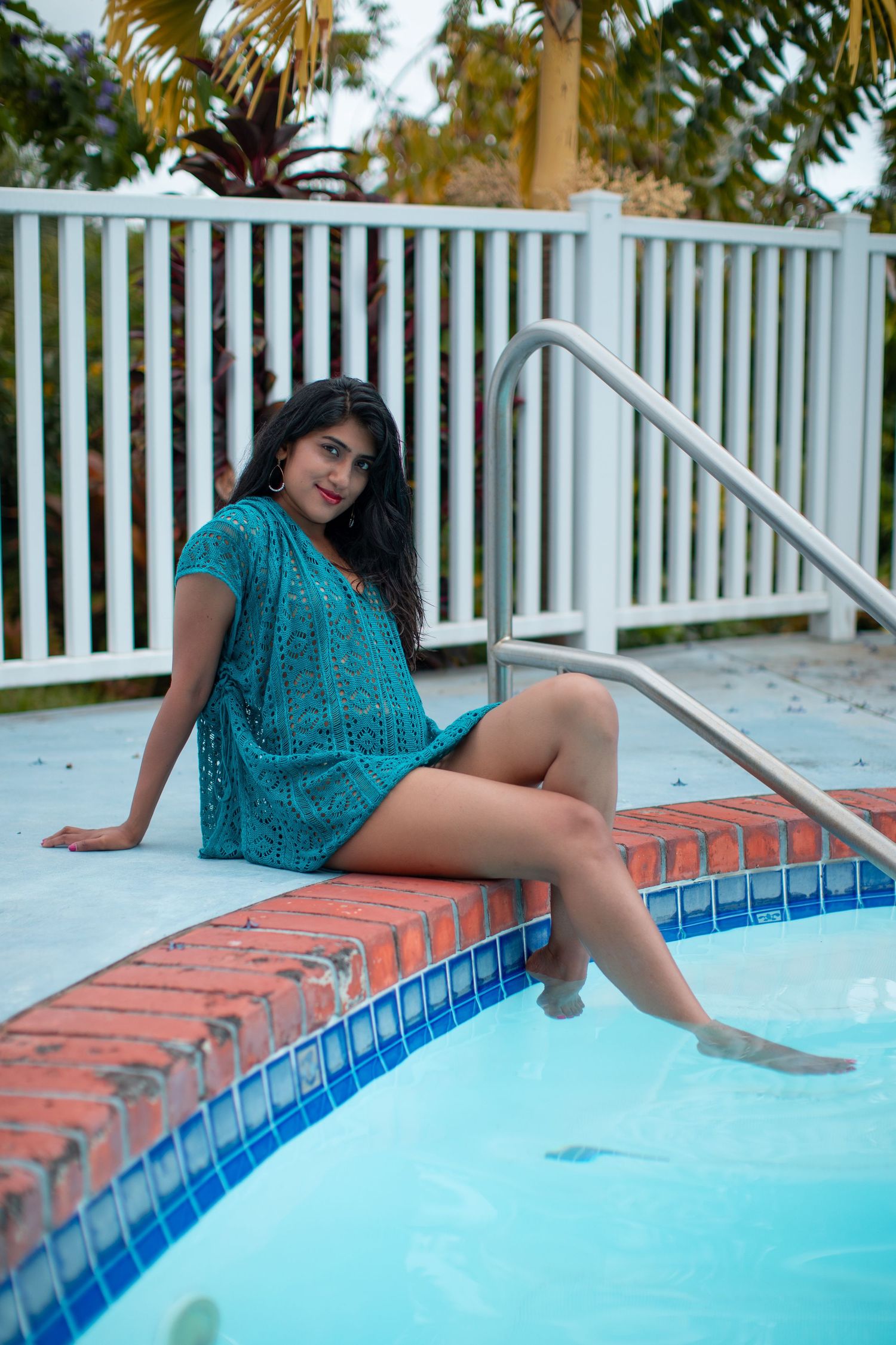 Relaxed poolside portrait in a turquoise dress with white pool railing.