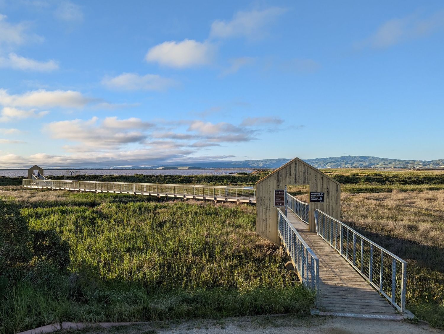 San Jose Alviso Marina park - wooden boardwalk extends through natural grassland with mountains visible in the distance.