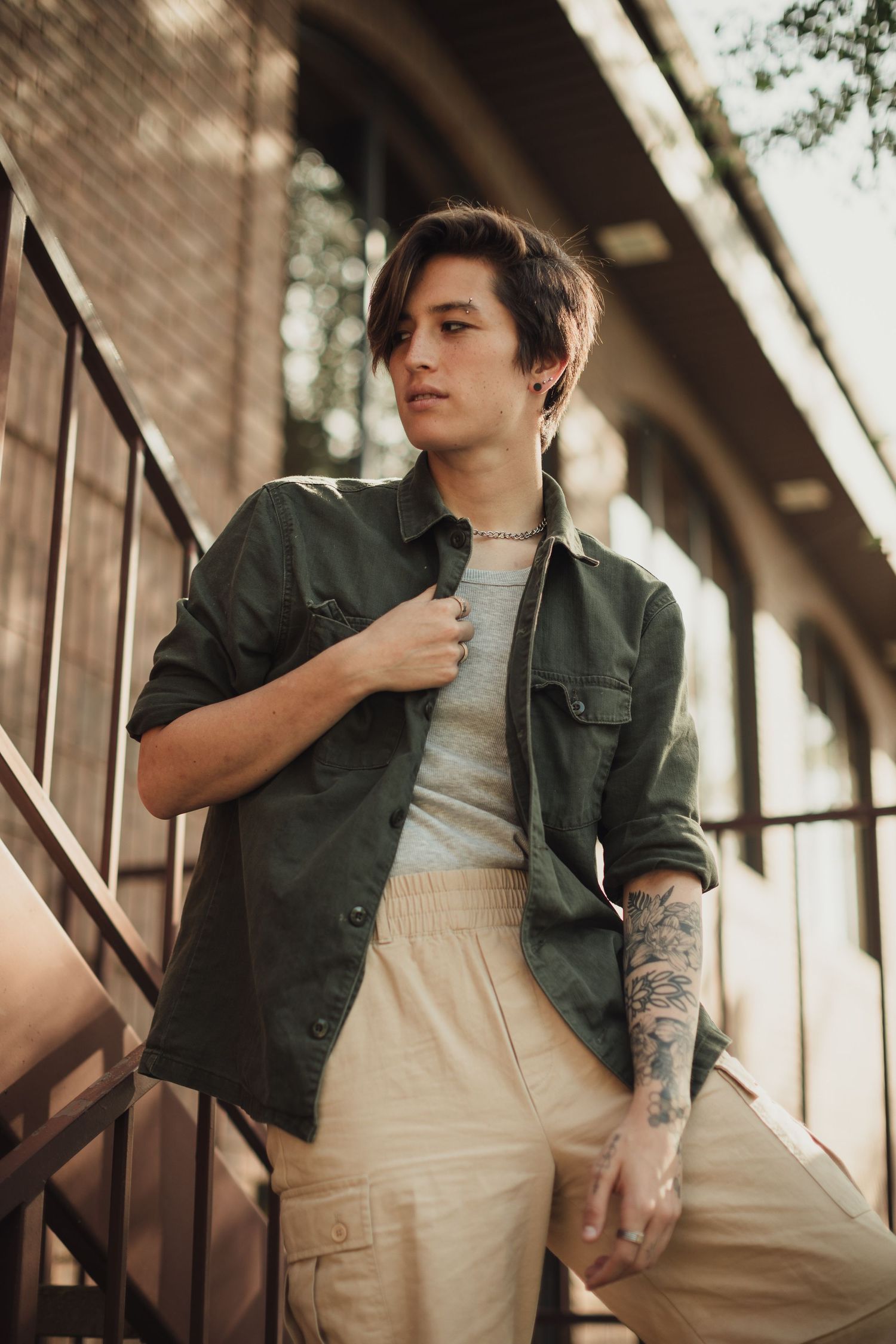 Outdoor fashion shoot featuring green jacket and tattoo details against brick wall.