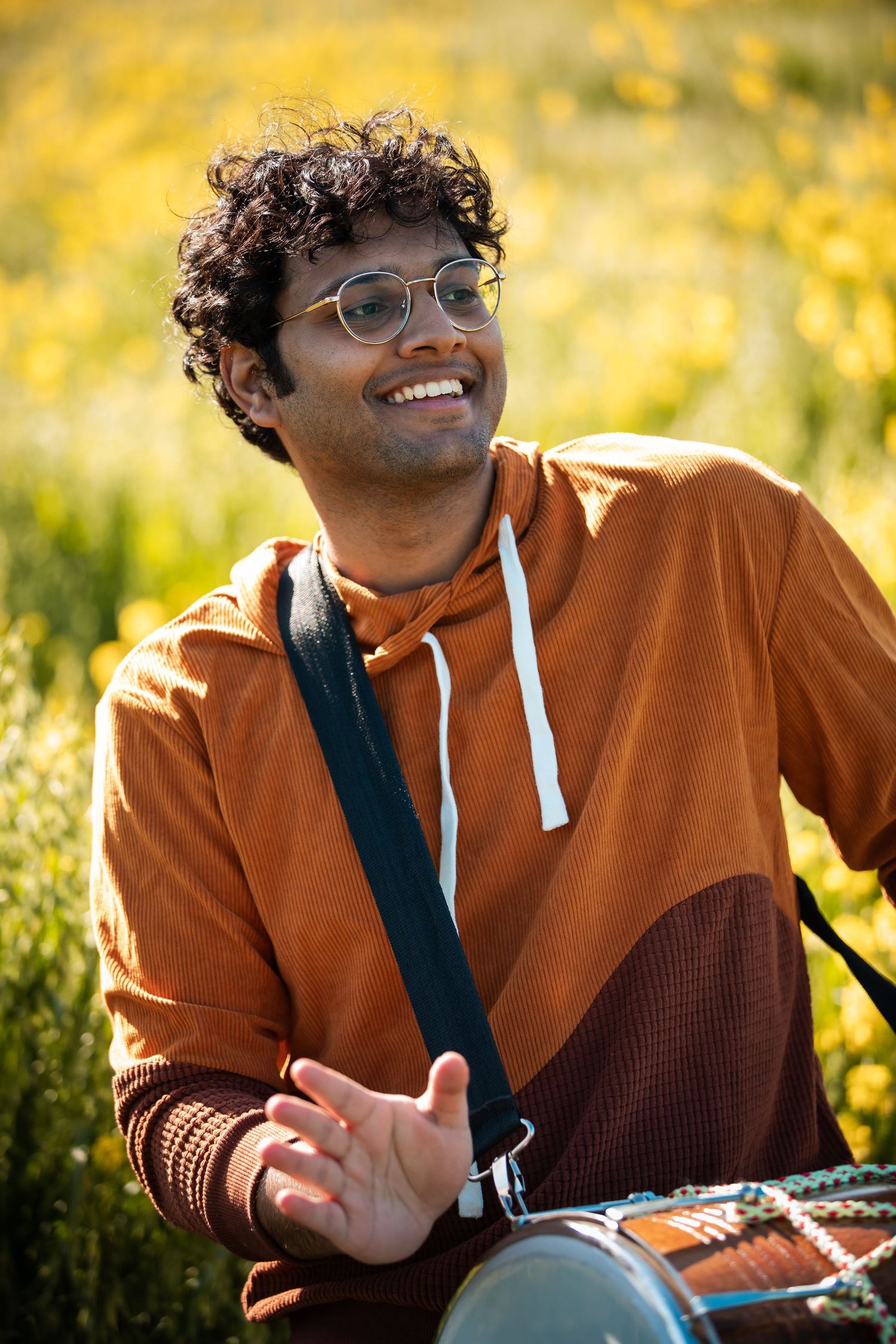 Person wearing orange hoodie and glasses smiles joyfully in golden sunlit field.