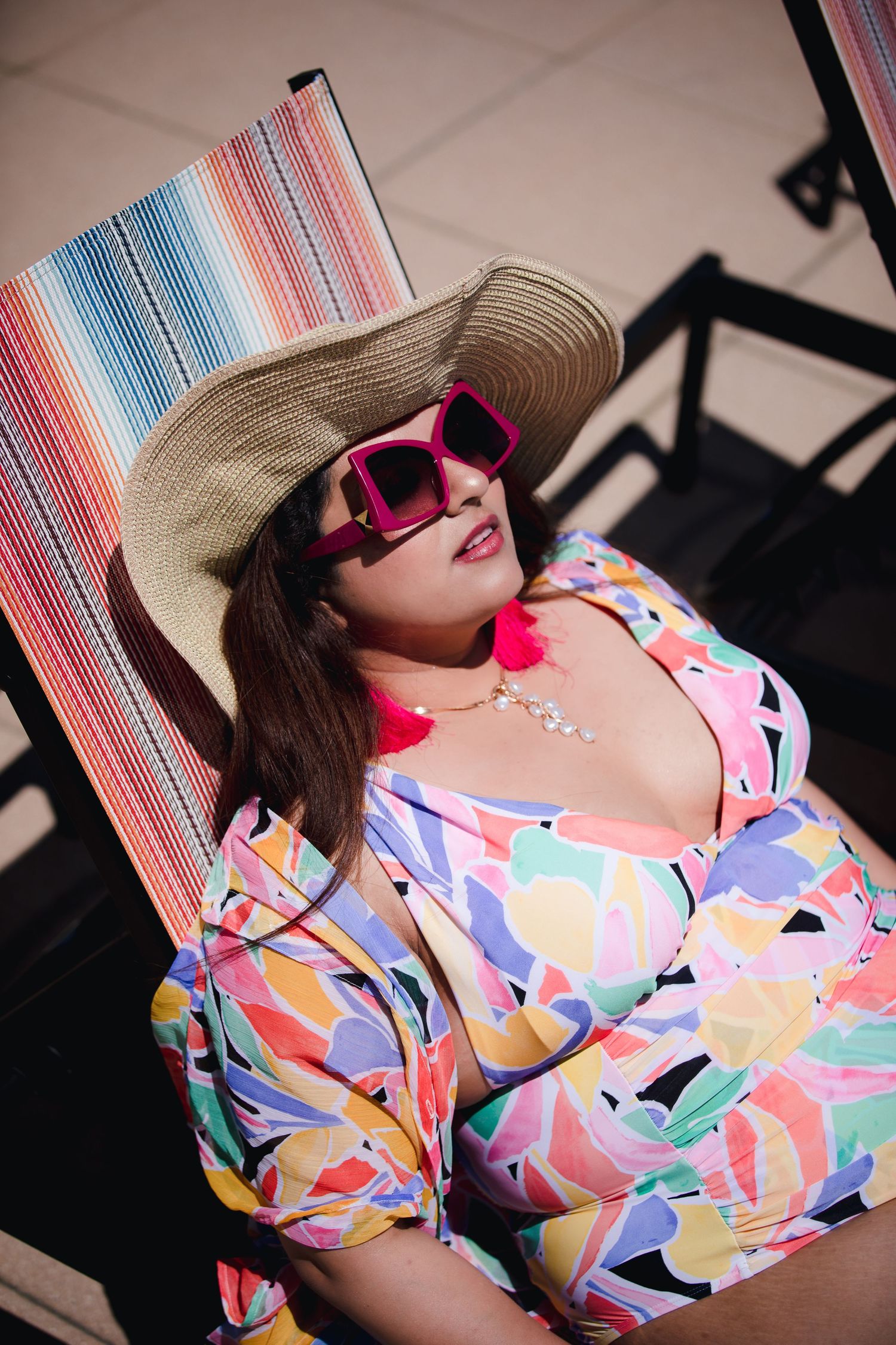 Person in colorful geometric print swimsuit and sunhat lounges by pool.