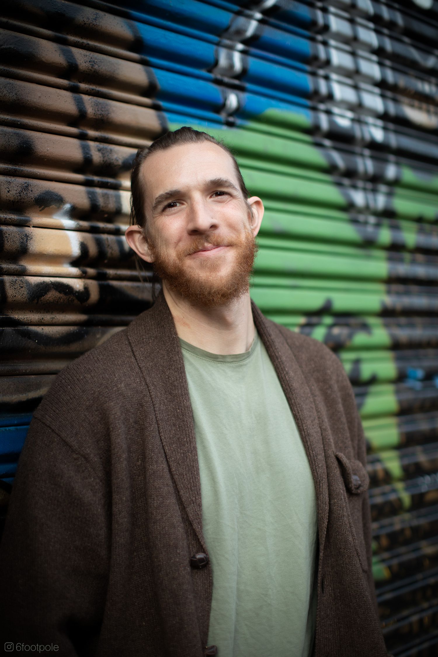 Series of casual portraits against urban graffiti background with brown jacket and sage green shirt.