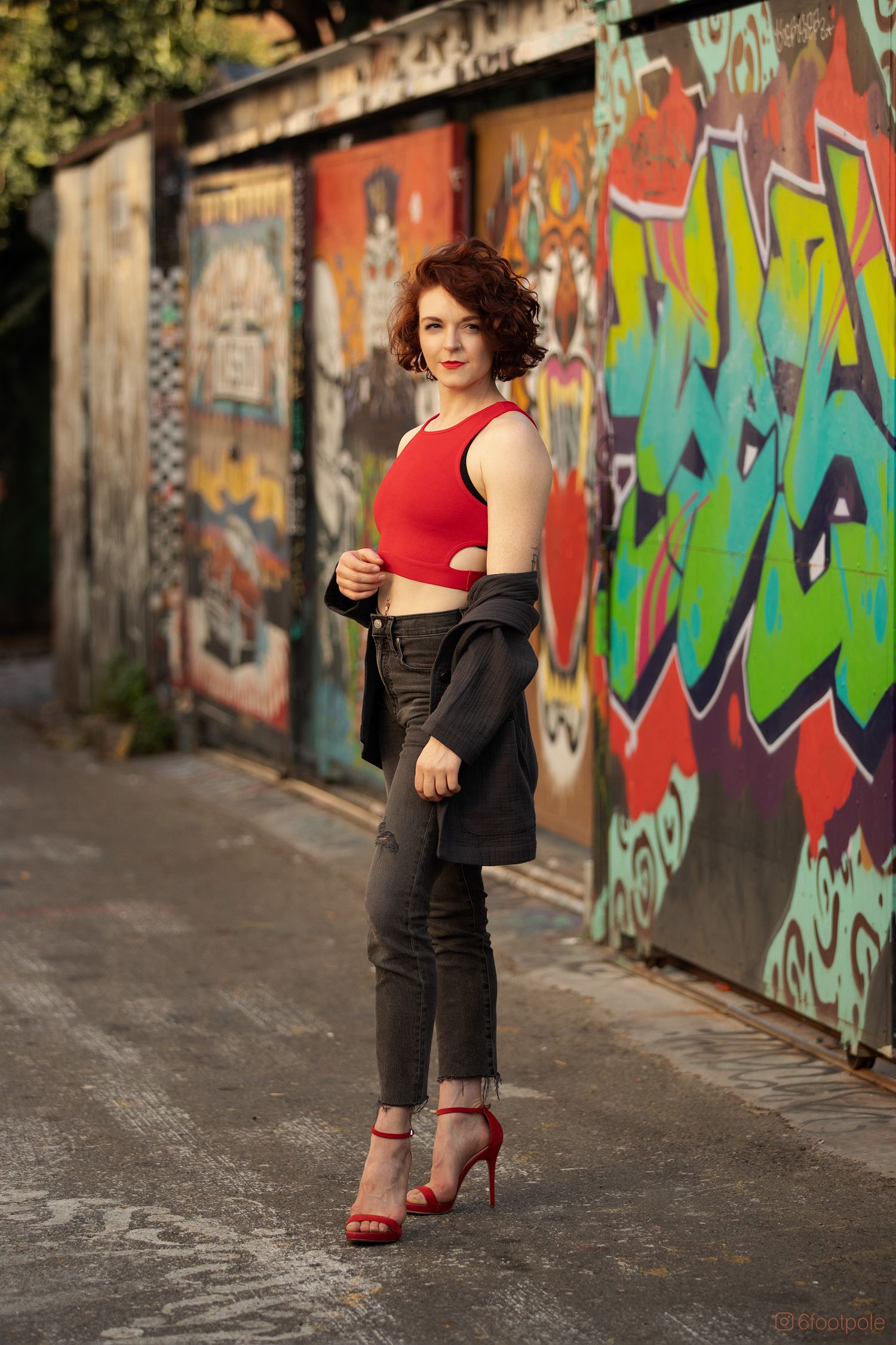 Stylish urban photoshoot featuring red crop top and high heels against colorful graffiti wall backdrop.