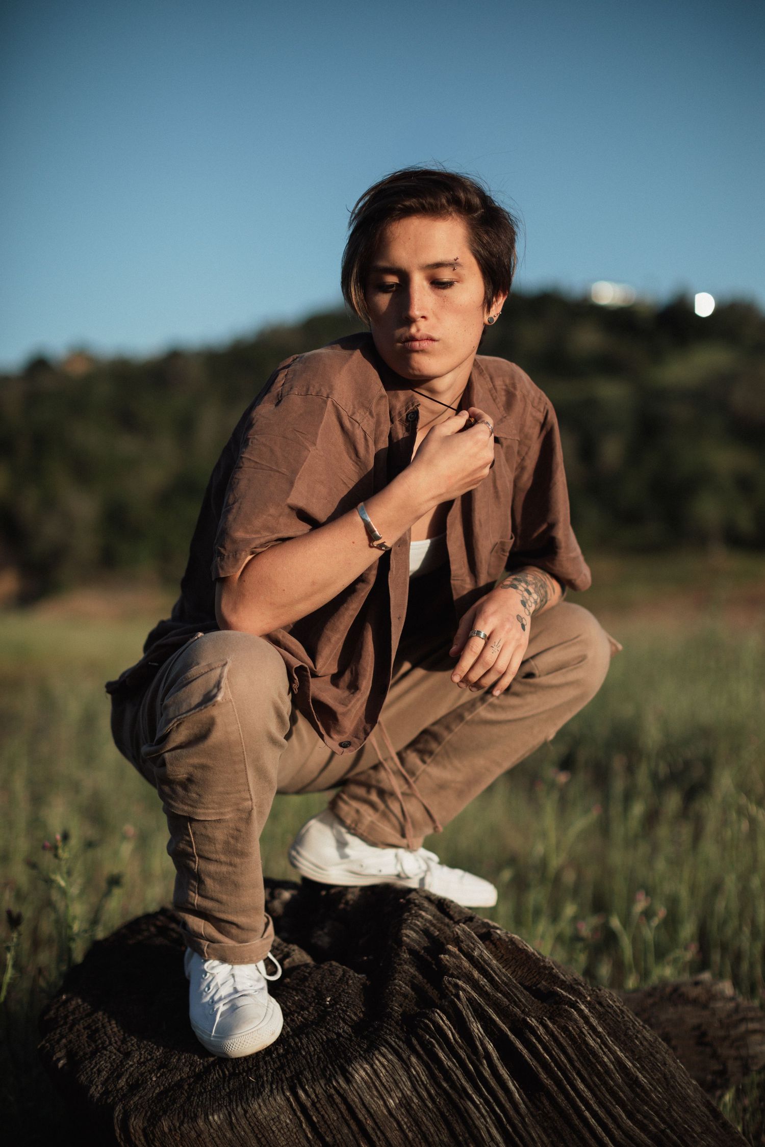 Person in casual wear crouches on rocky surface during sunset outdoors.