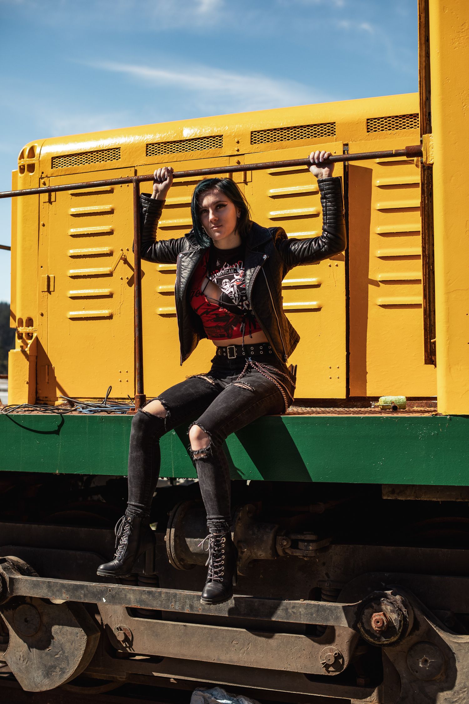 Person in black sitting on yellow train car in casual urban photoshoot.