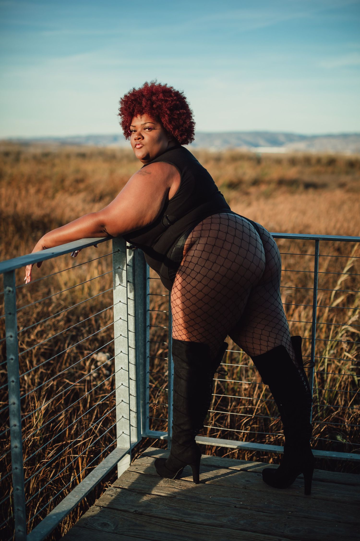 Expressive fashion photography on wooden deck with natural grassland backdrop.