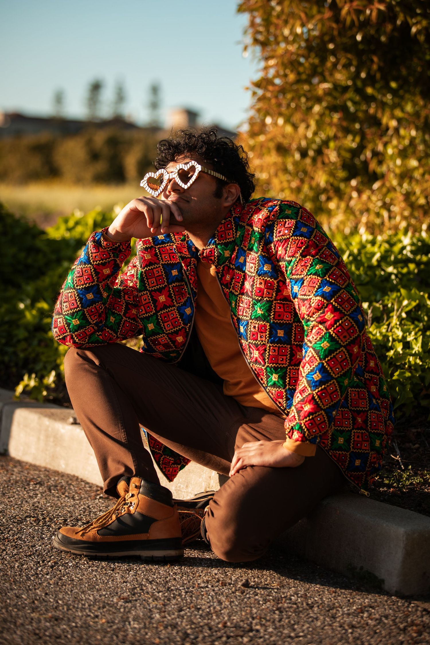 Figure in vibrant print shirt crouches on ground during golden hour photography session.