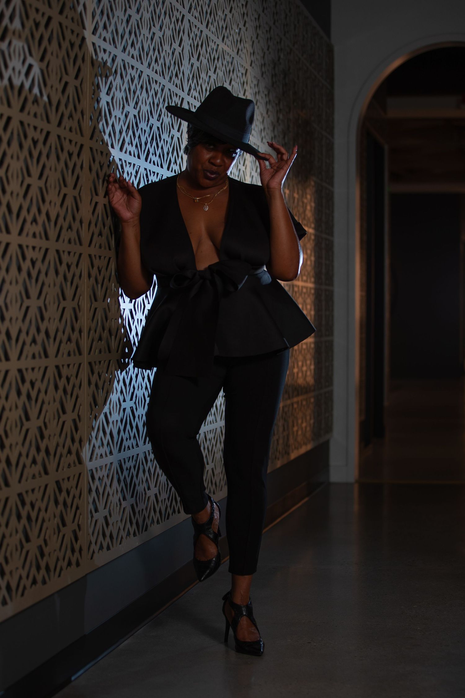 Model in black outfit poses dramatically in dimly lit hallway.