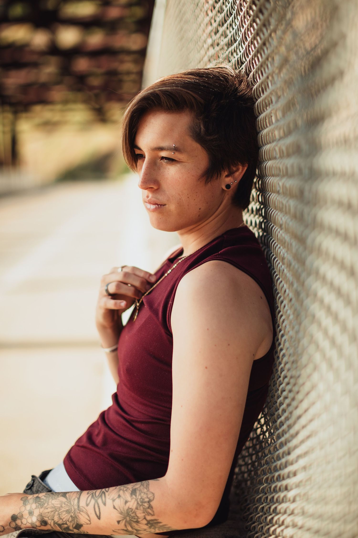 Person in maroon sleeveless shirt leans against chain link fence in outdoor setting.