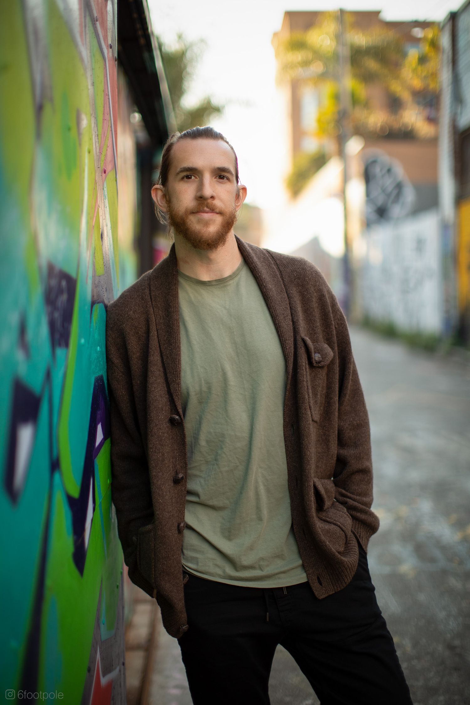 Casual portrait in brown cardigan and olive shirt against street art backdrop.