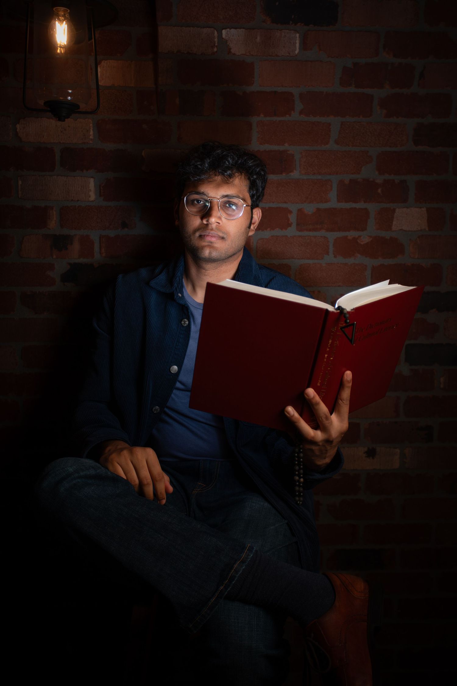 Person reading red book in dimly lit room with brick wall background.