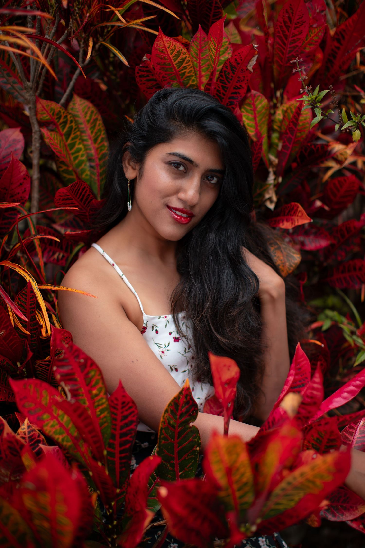 Fashion portrait with white floral dress against backdrop of red tropical foliage.
