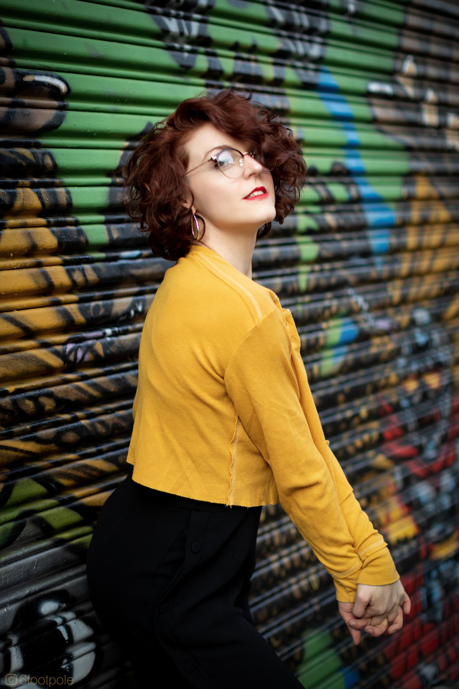 Fashion portrait against colorful graffiti wall featuring bright yellow jacket and dramatic pose.