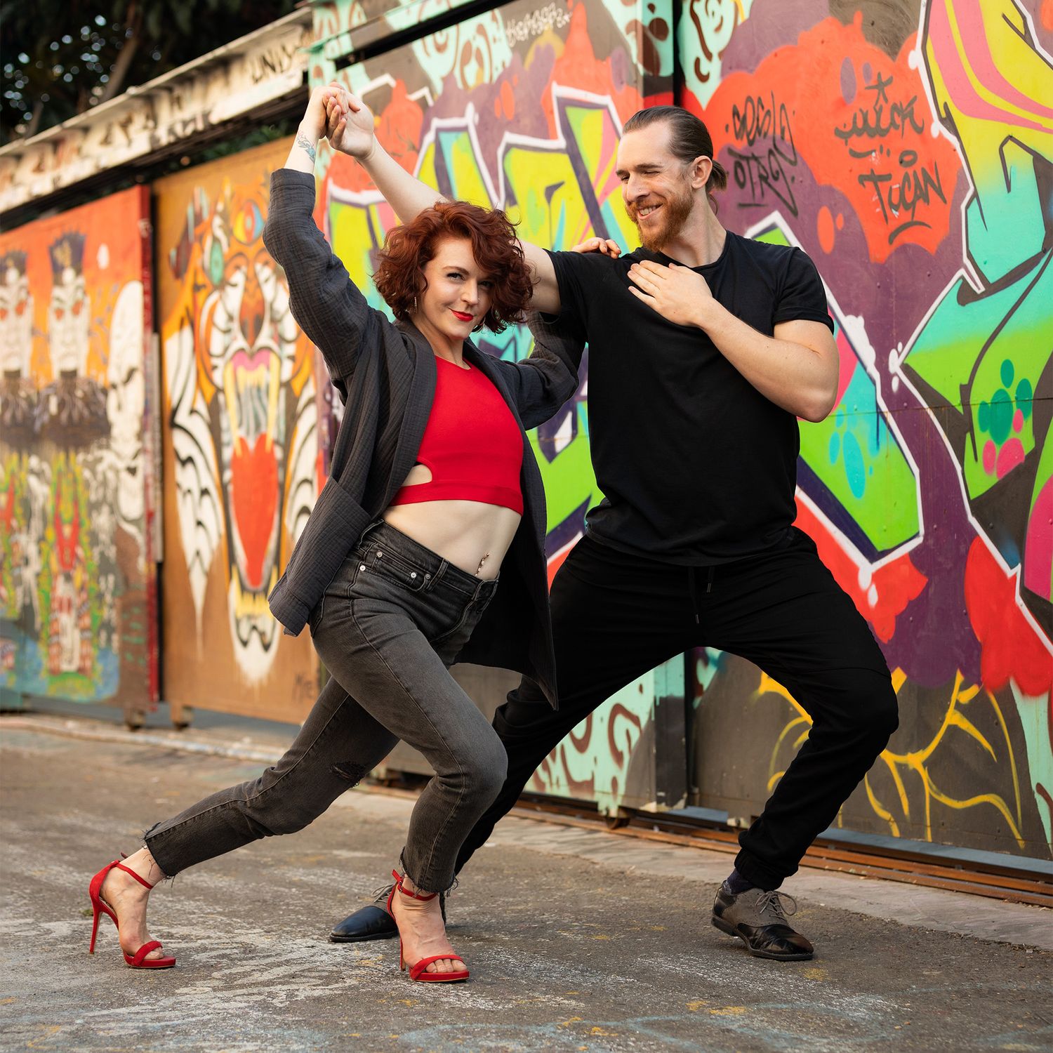 Dancers in black athletic wear perform dynamic movements against a vibrant graffiti wall backdrop.