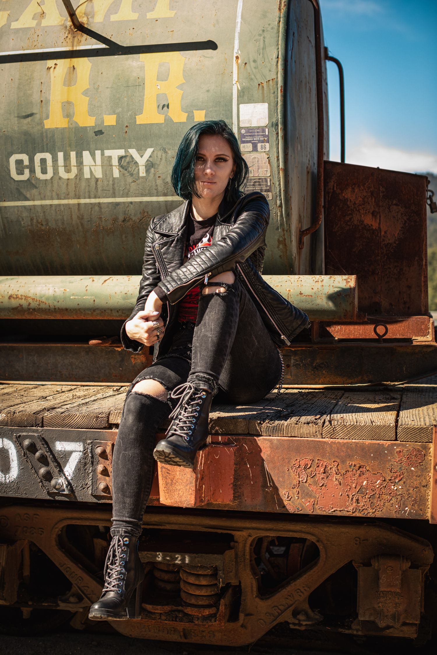 Person in leather jacket and boots sitting on rustic train car with vintage lettering.
