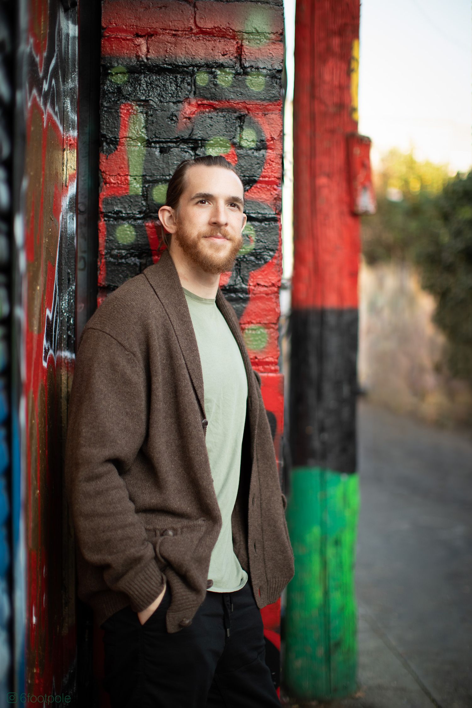 Portrait series against a red brick wall with brown coat and light colored shirt in natural lighting.