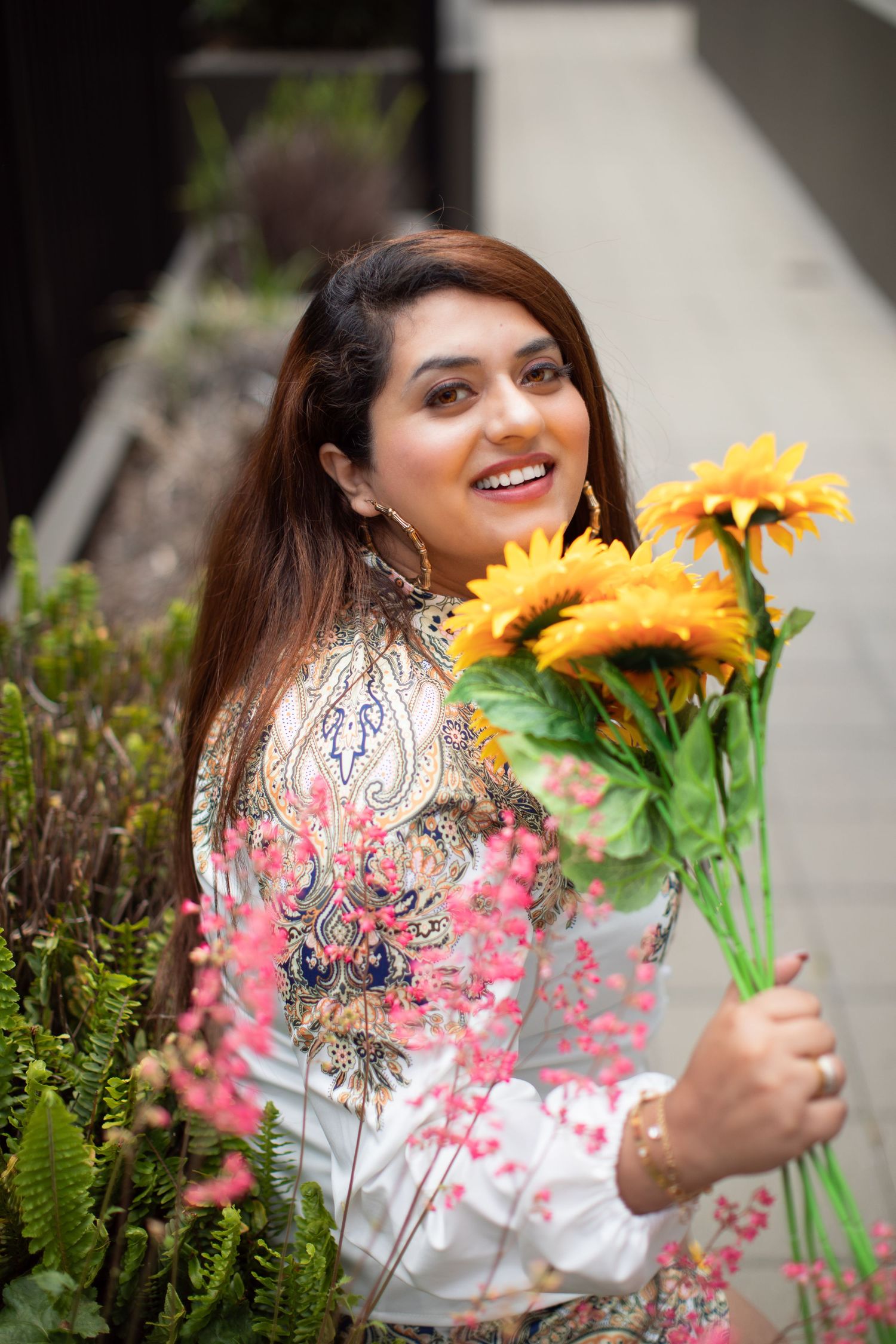 Spring fashion photography with sunflowers and floral embroidered clothing against pink bokeh effects.