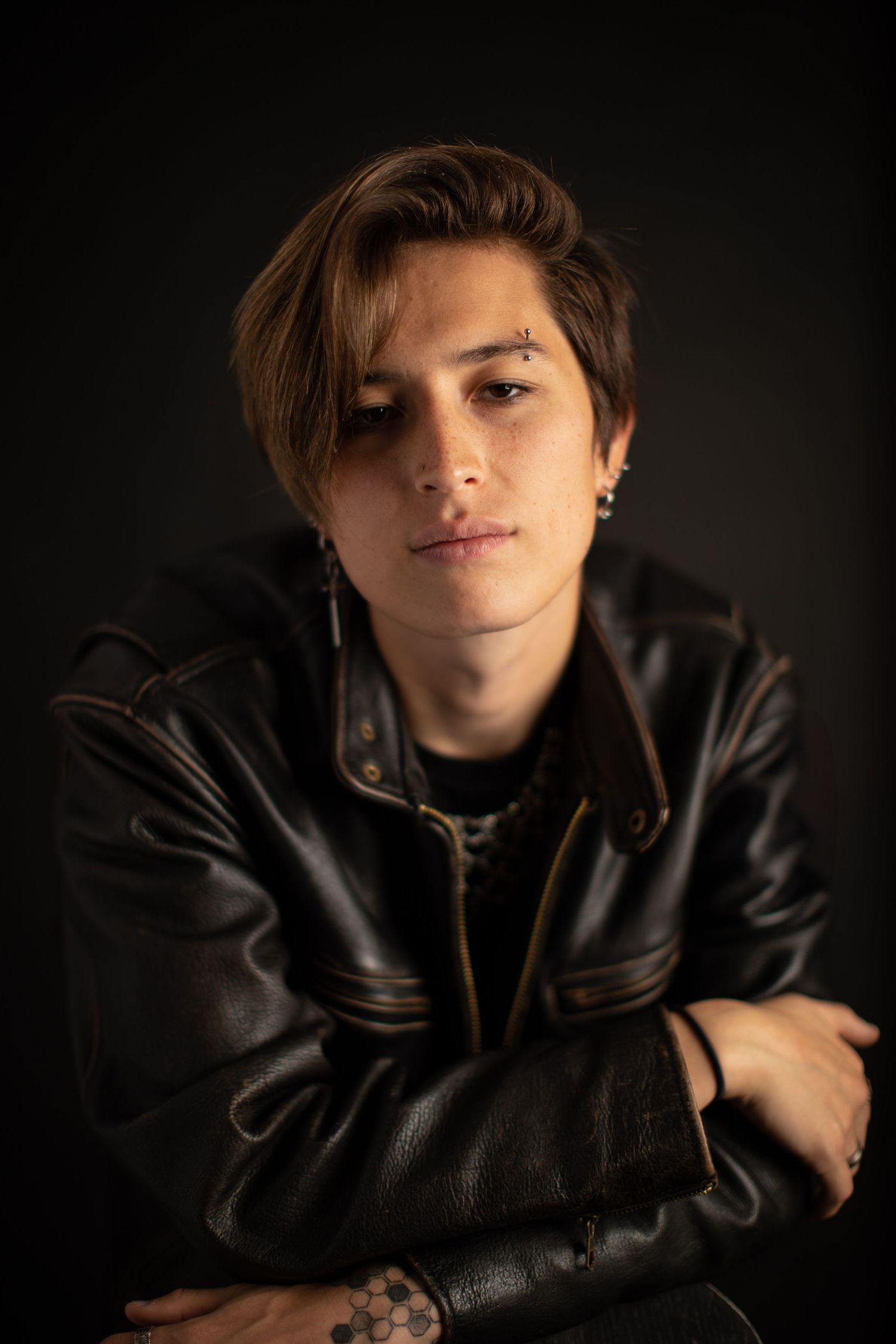 Dramatic portrait in black leather jacket against dark background with moody lighting.
