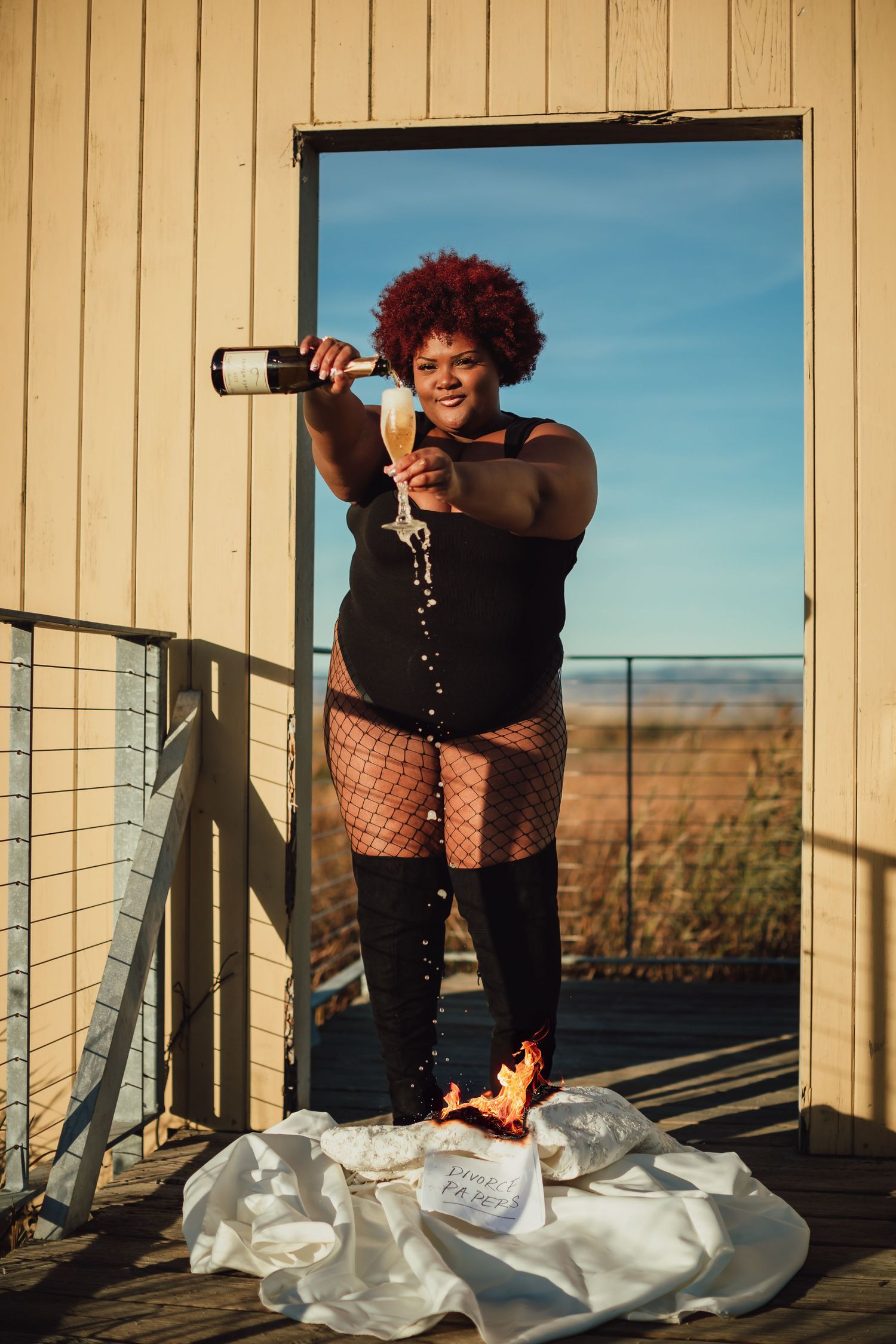 Creative portrait of person in fishnet stockings popping champagne on outdoor deck.