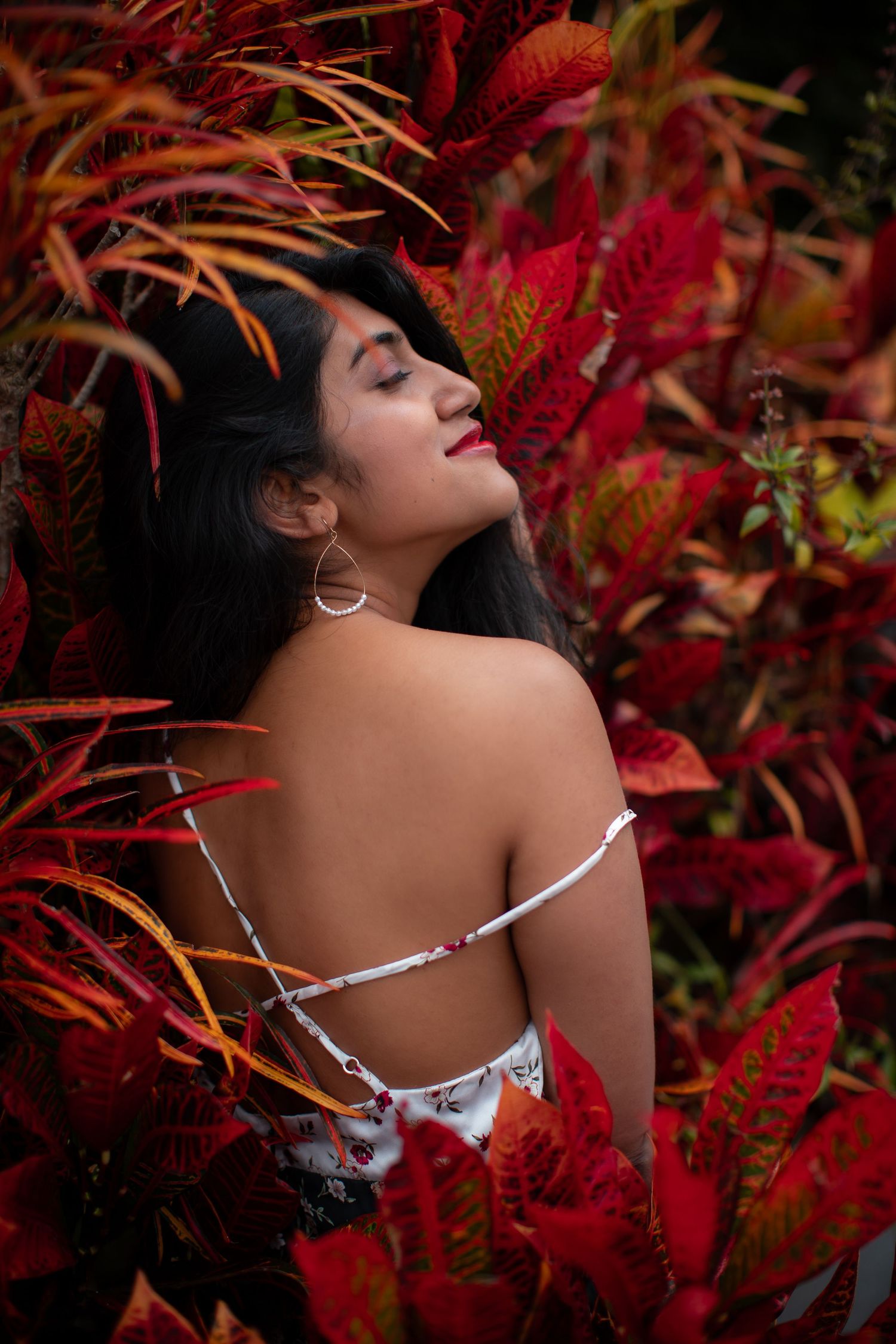 Dramatic portrait among vibrant red tropical plants with white dress strap detail.