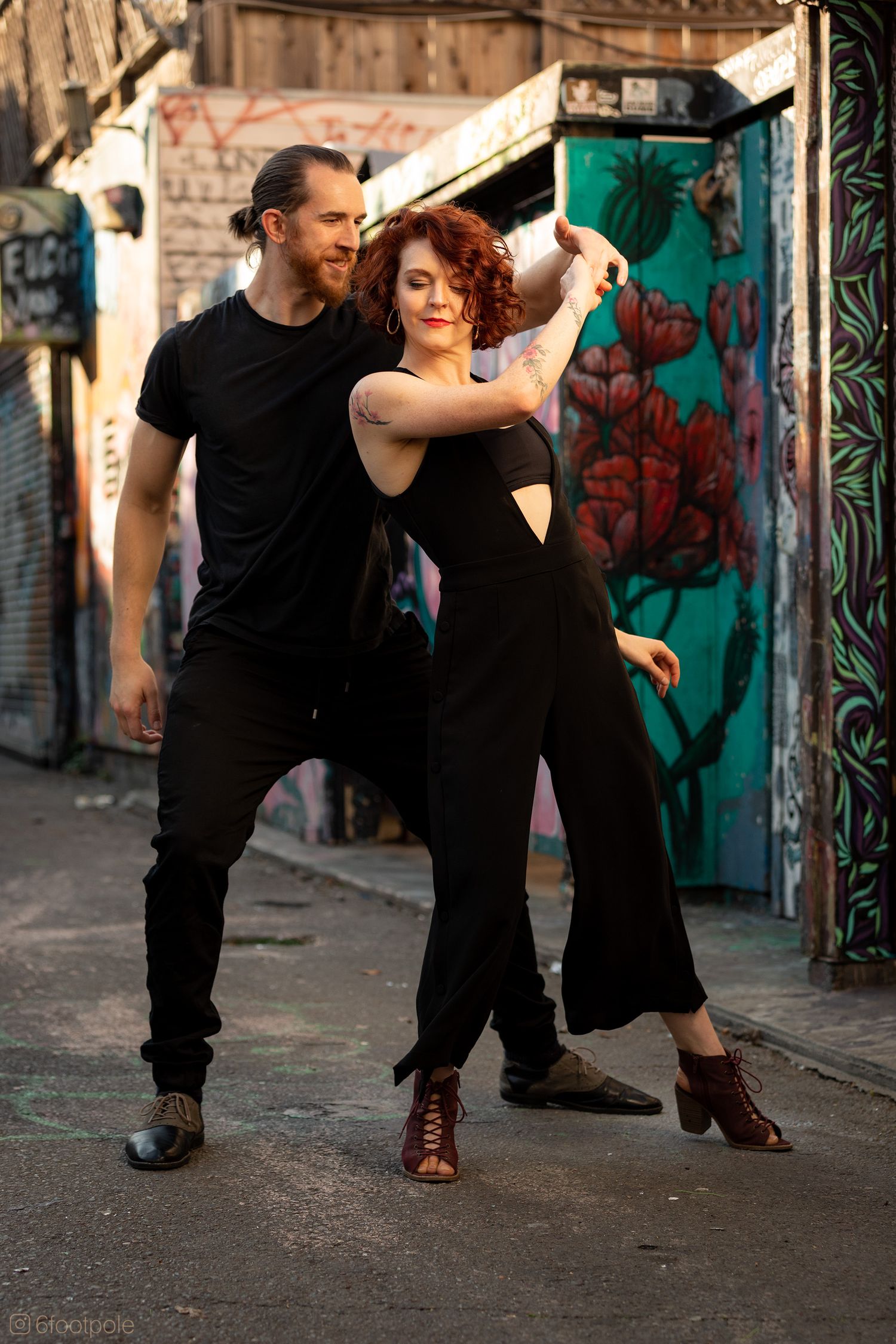 Dance partners practicing in alley with street art backdrop and dramatic lighting.