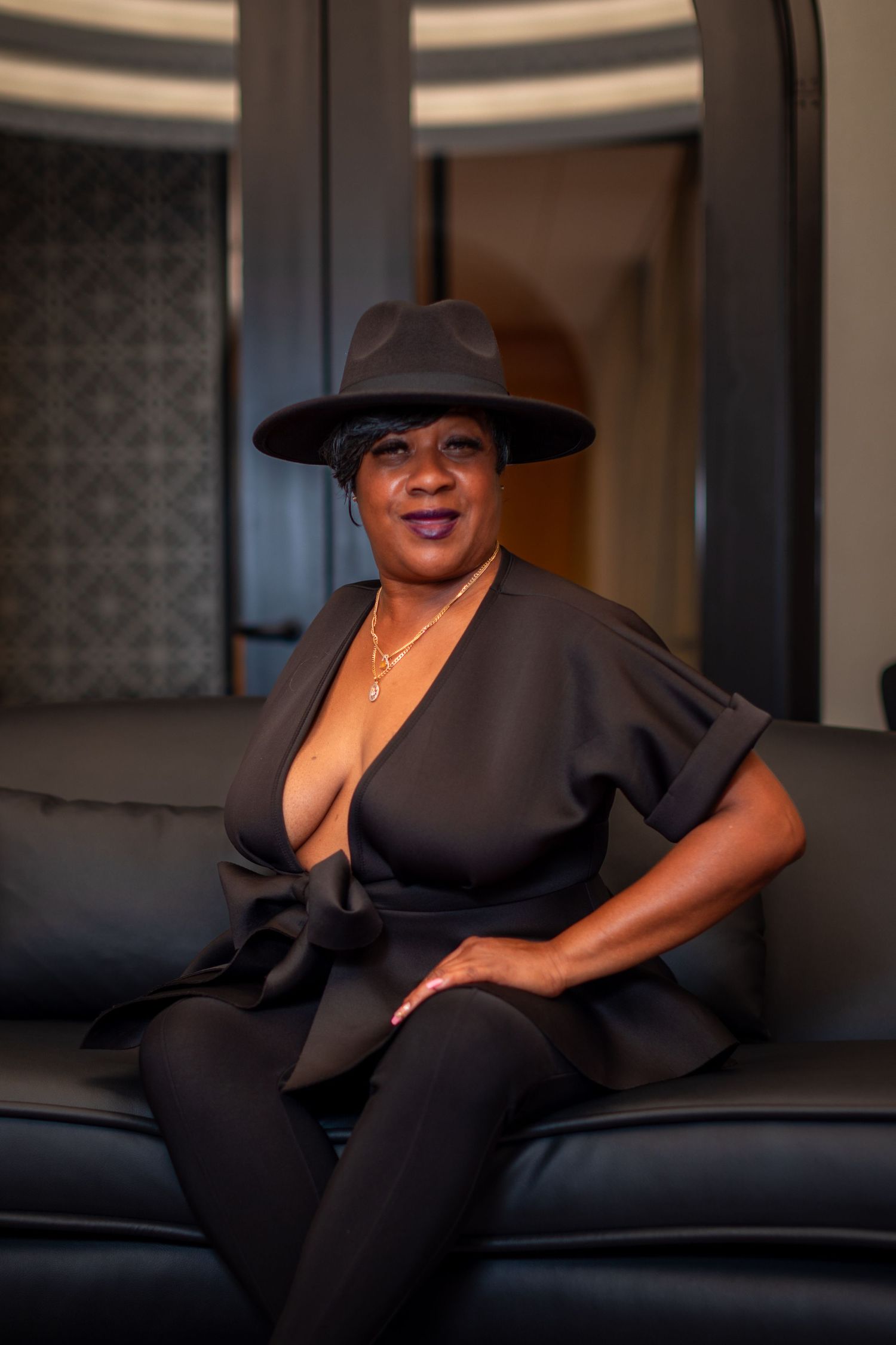 Stylish portrait session on leather sofa with dramatic lighting and hat accessory.