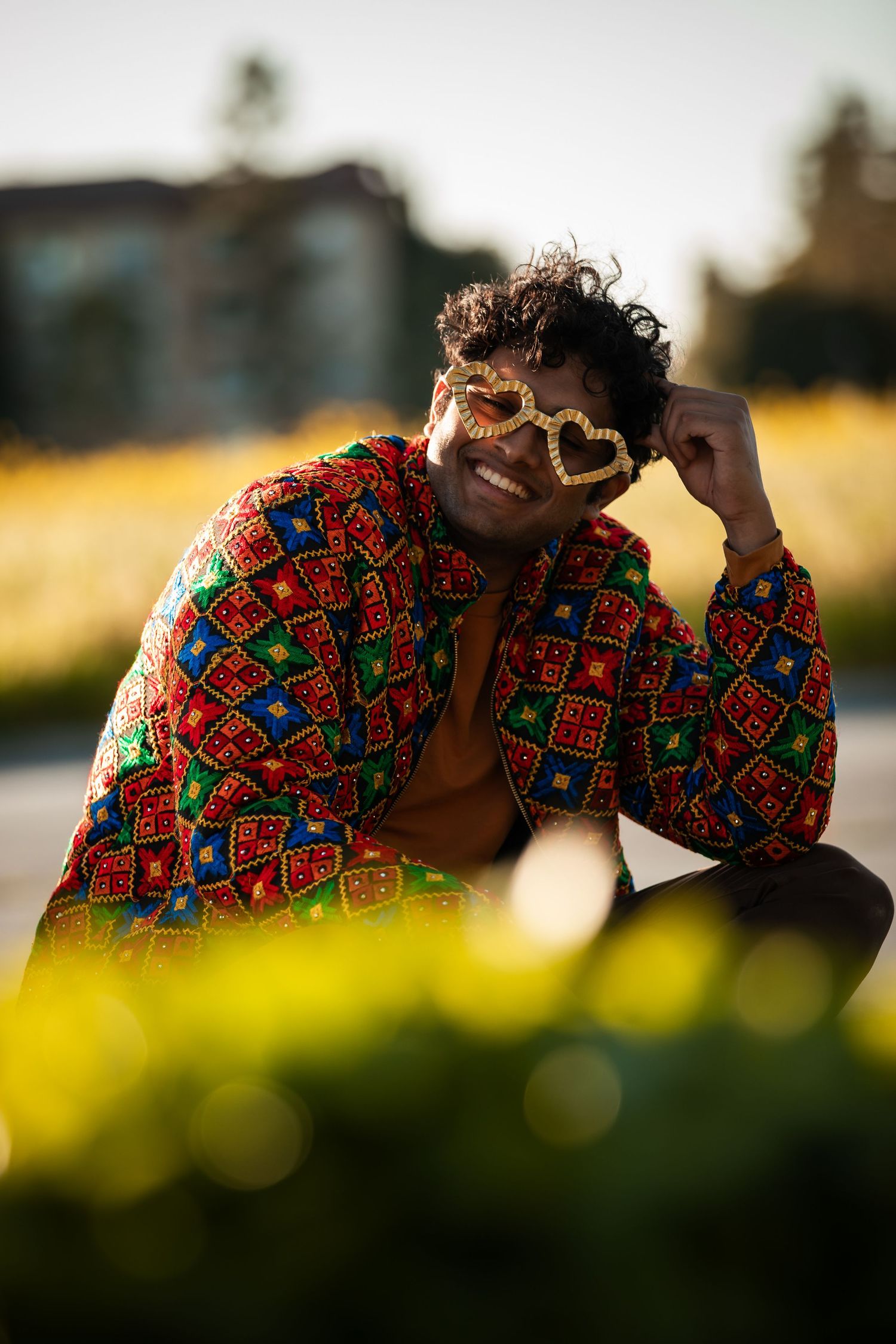 Figure in vibrant African print shirt reclines on ground with blurred yellow flowers in foreground.