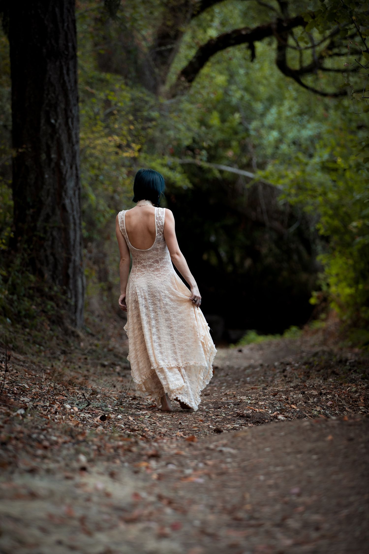 Ethereal figure in white dress walking away on a shadowy forest path.