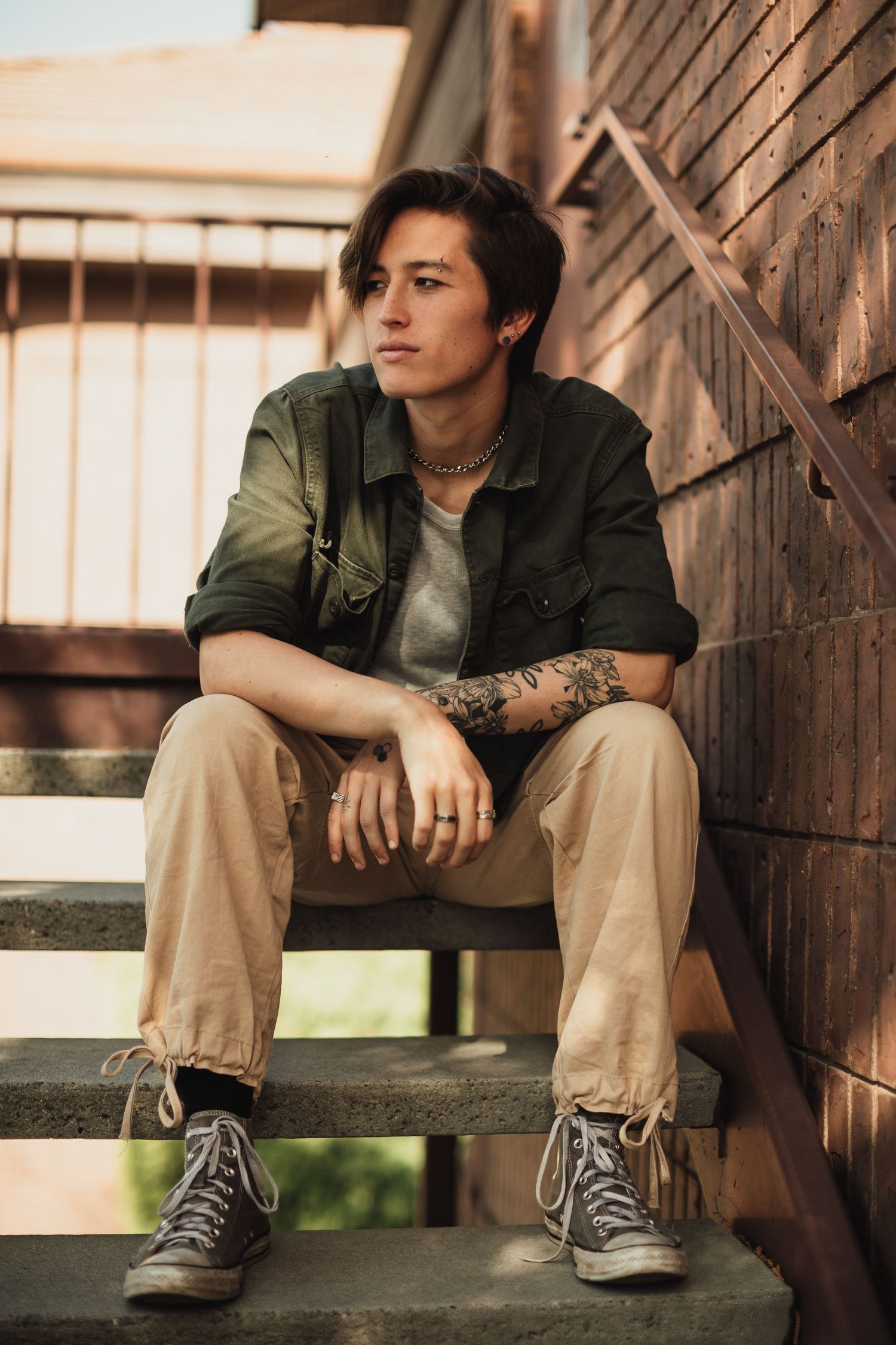 Person in green jacket and khakis sitting on wooden steps outdoors.