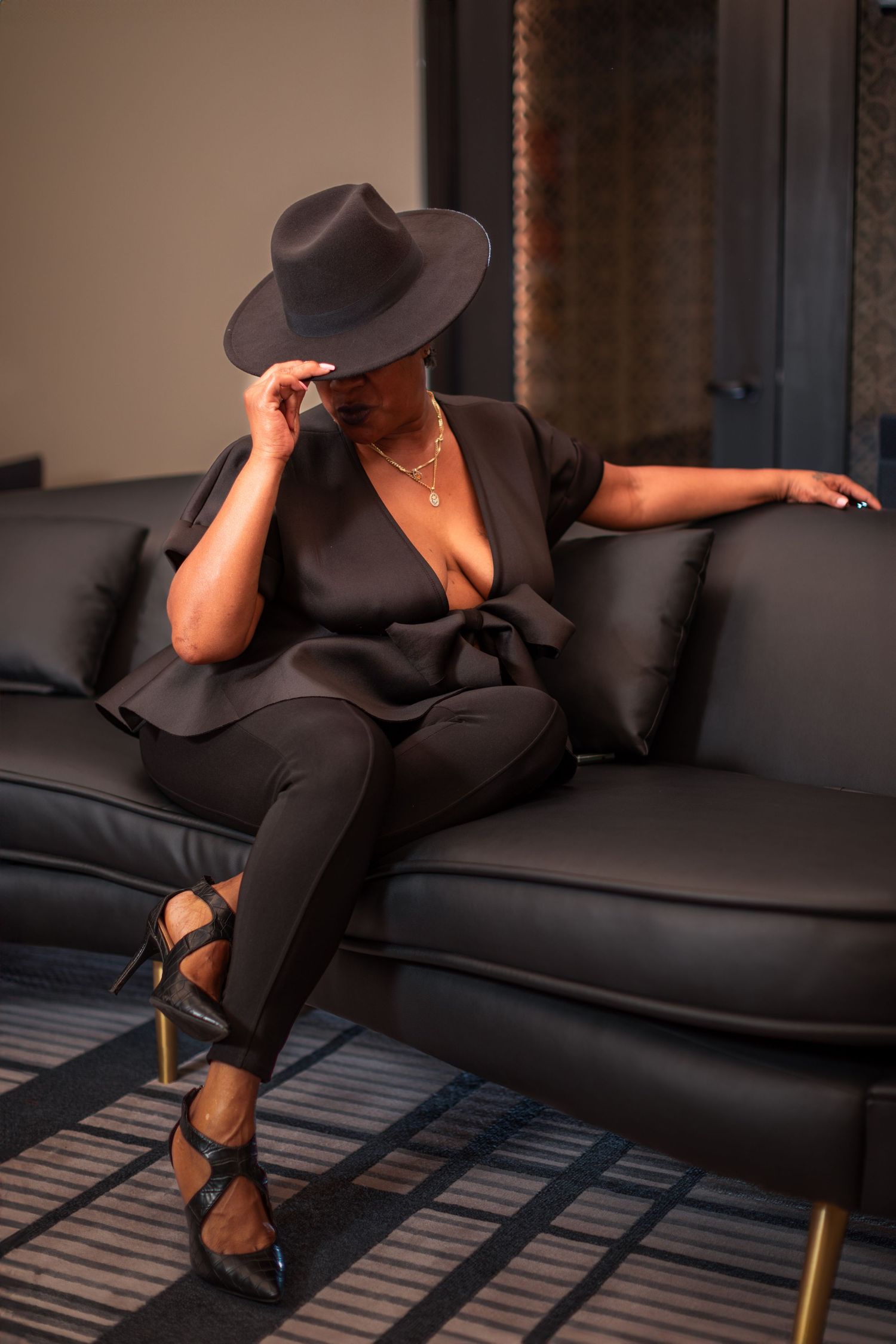 Fashion editorial style poses on modern black leather couch with hat.