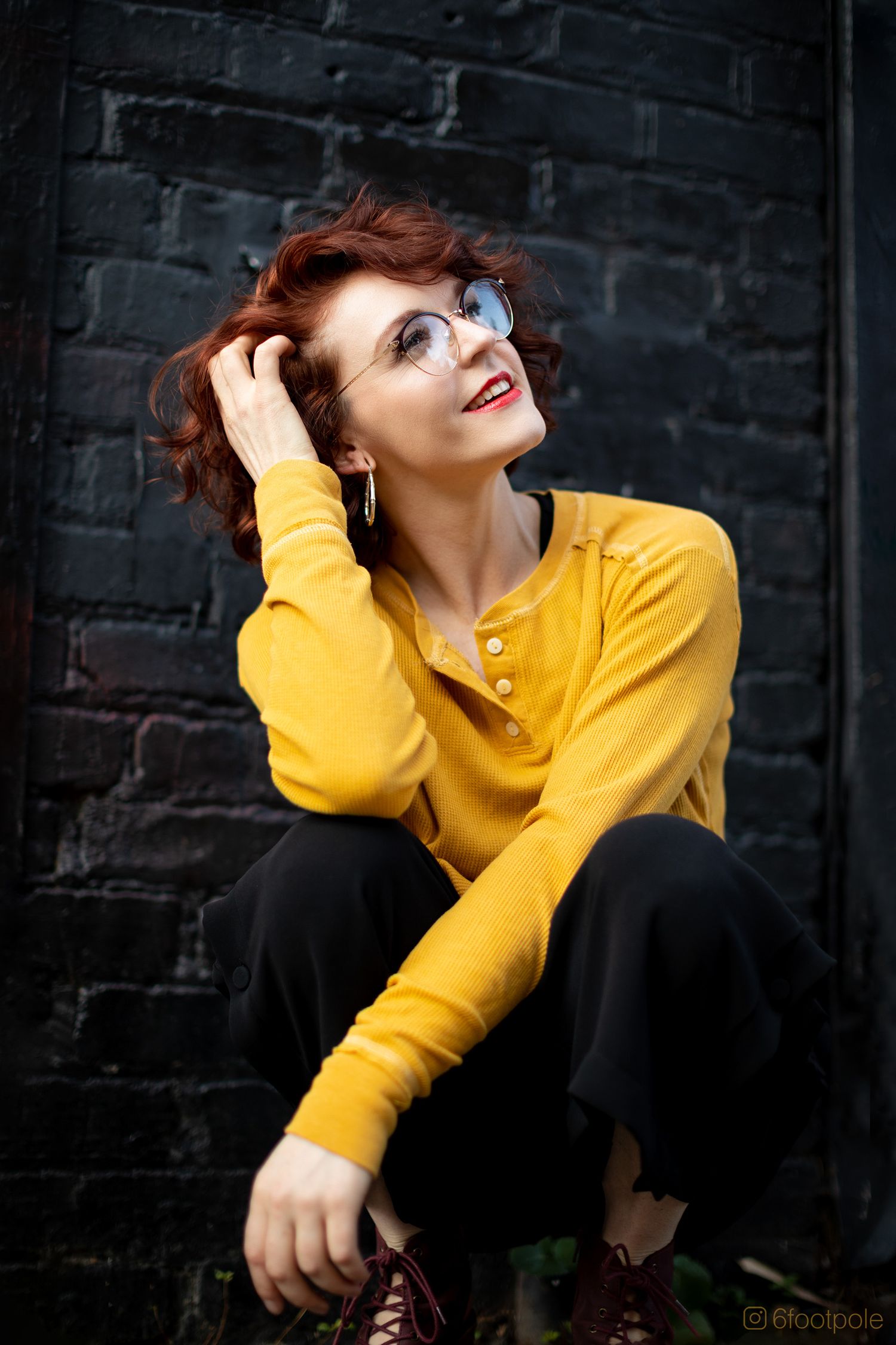 Dramatic portrait against dark brick wall featuring bright yellow sweater and expressive pose.