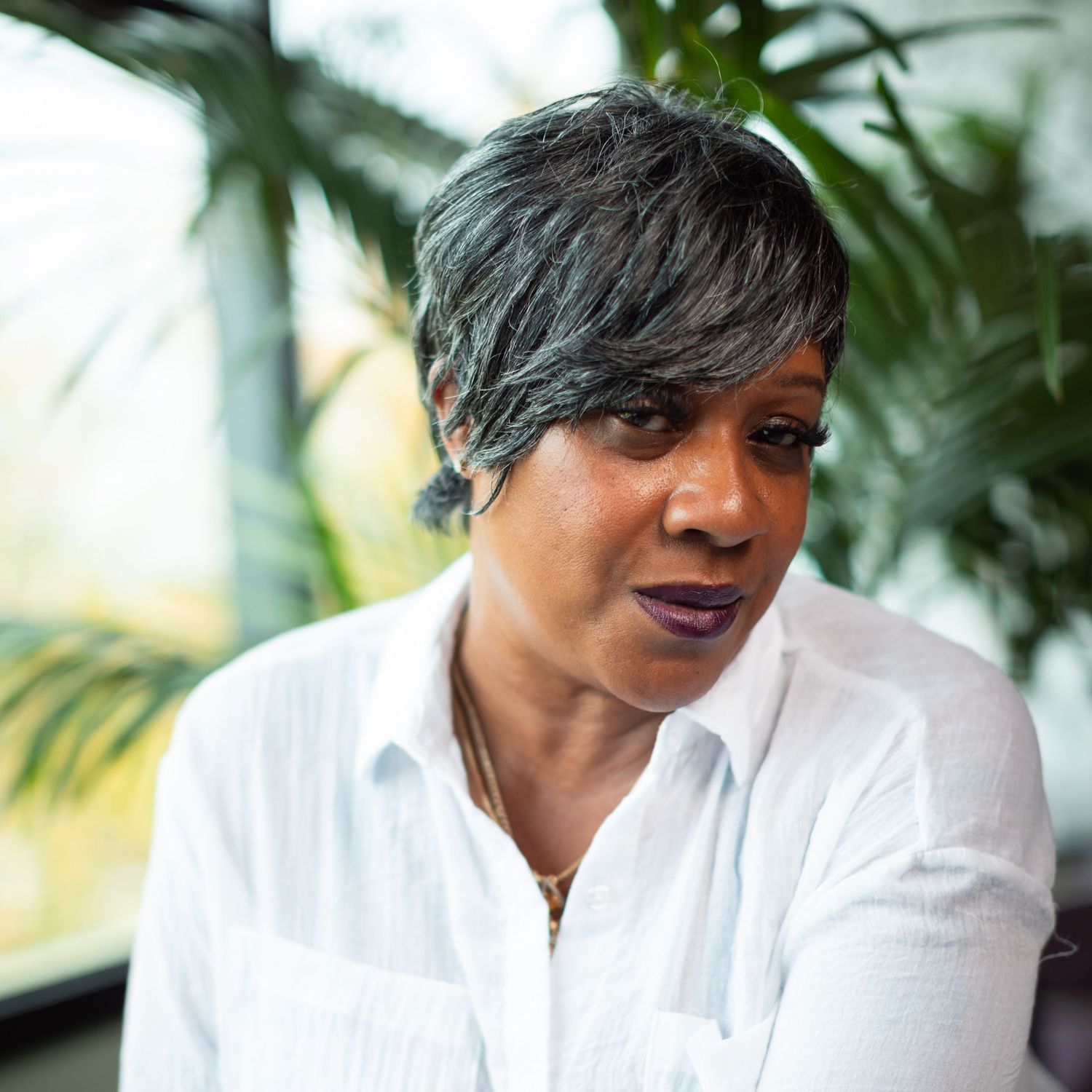 Professional portrait of someone with short gray hair wearing a white button-down shirt against a tropical palm background.