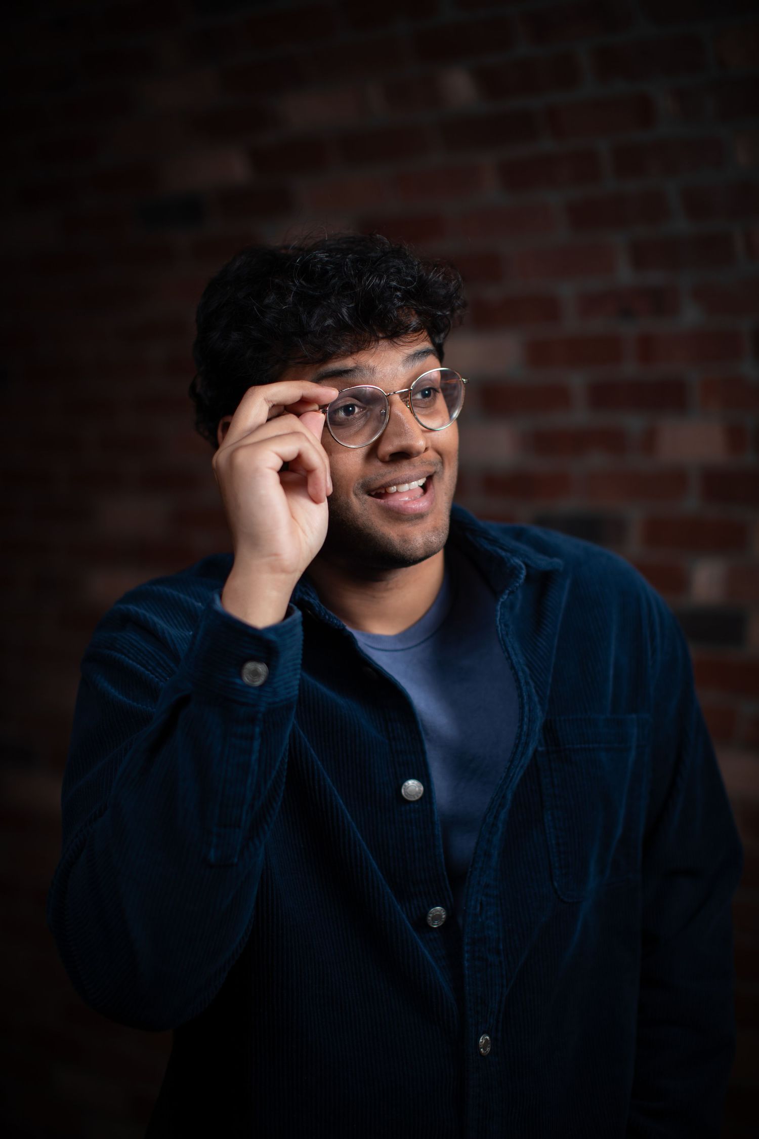 Close-up sequence of expressions while adjusting glasses against rustic brick background.