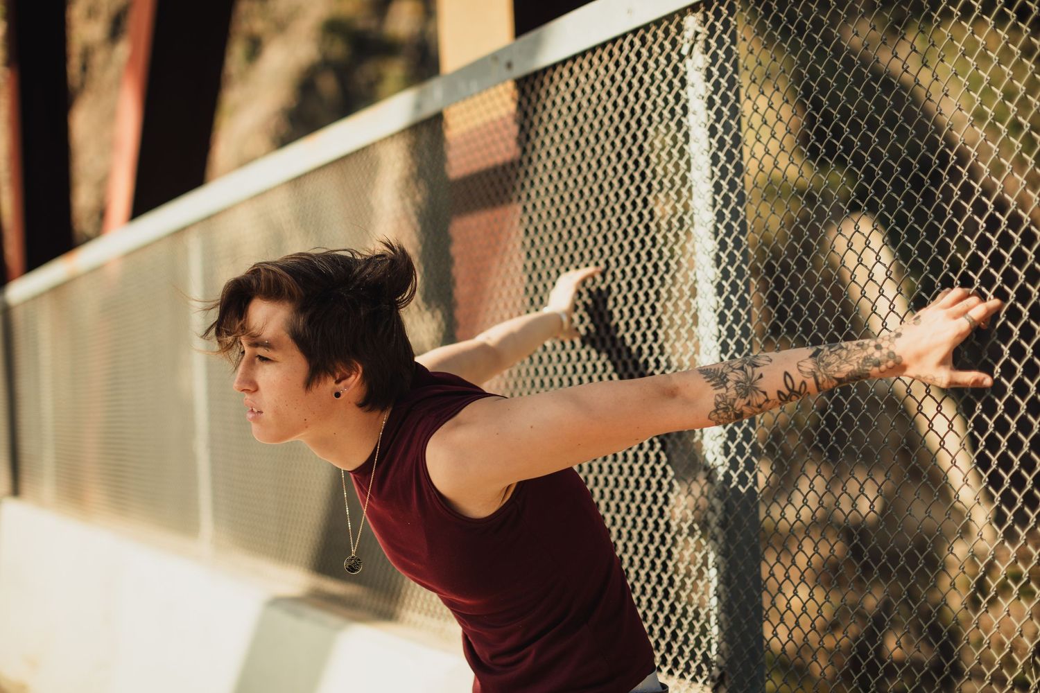Person in burgundy top poses against chain link fence in artistic portrait series.