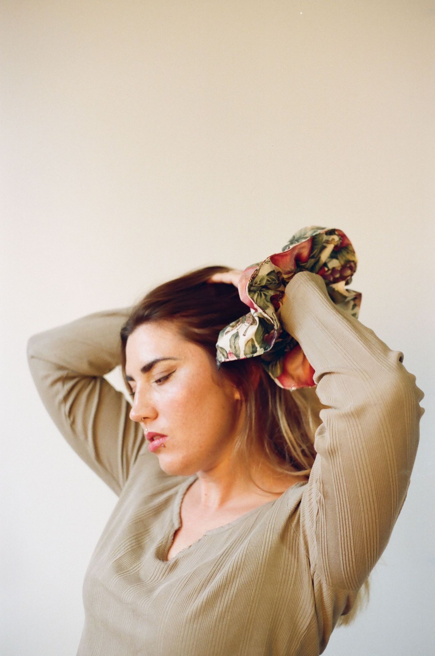 Woman in beige ribbed top styling her hair with a floral scrunchie against a light background.