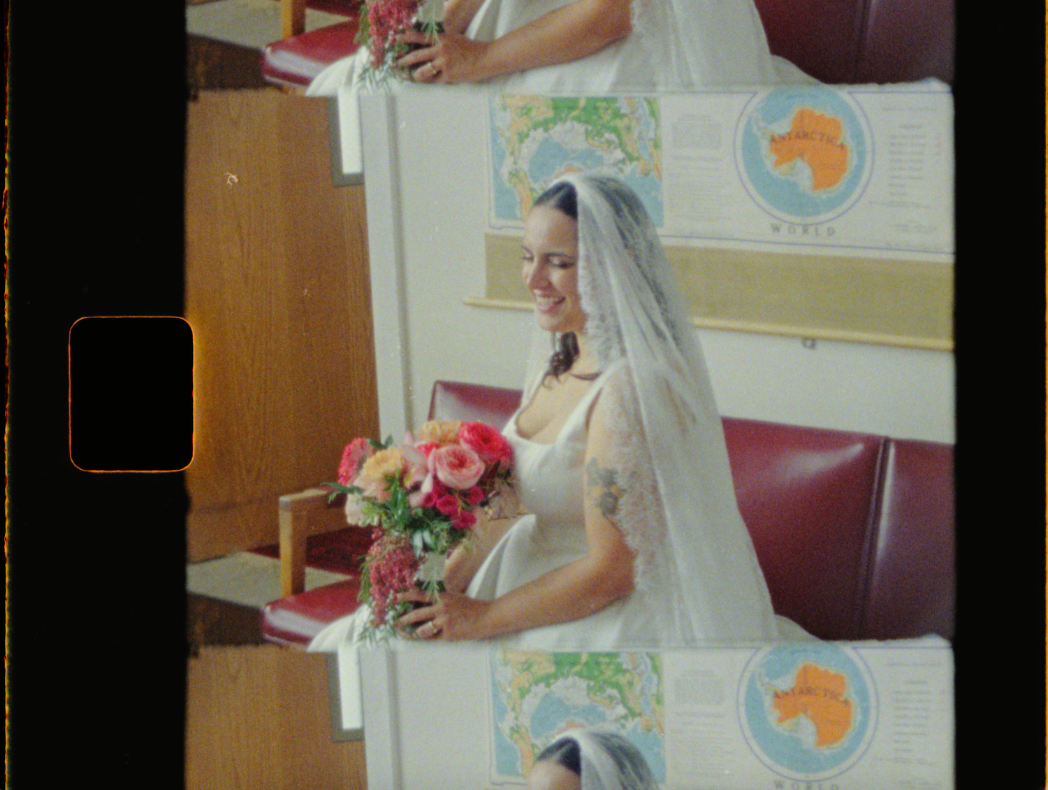 Bride in white wedding dress and veil holding pink floral bouquet, smiling inside a church decorated with banners.