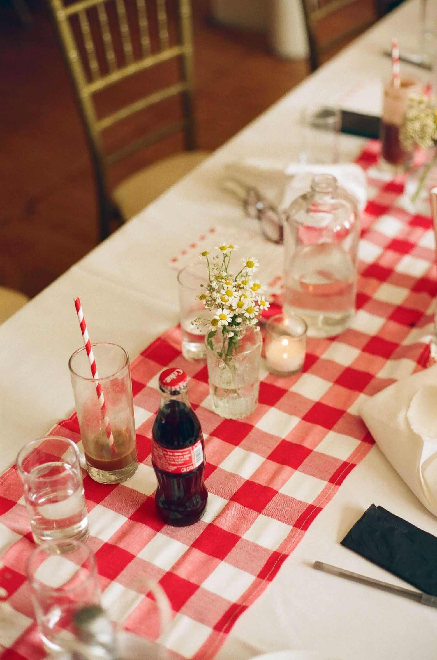 Red gingham table runner with Coca-Cola bottle, wildflowers, and striped straws at a festive dining table setting.
