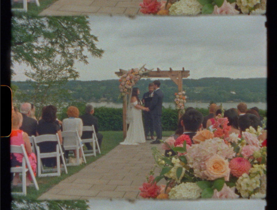 Outdoor wedding ceremony with couple at floral arch, guests seated on white chairs, overlooking scenic landscape.