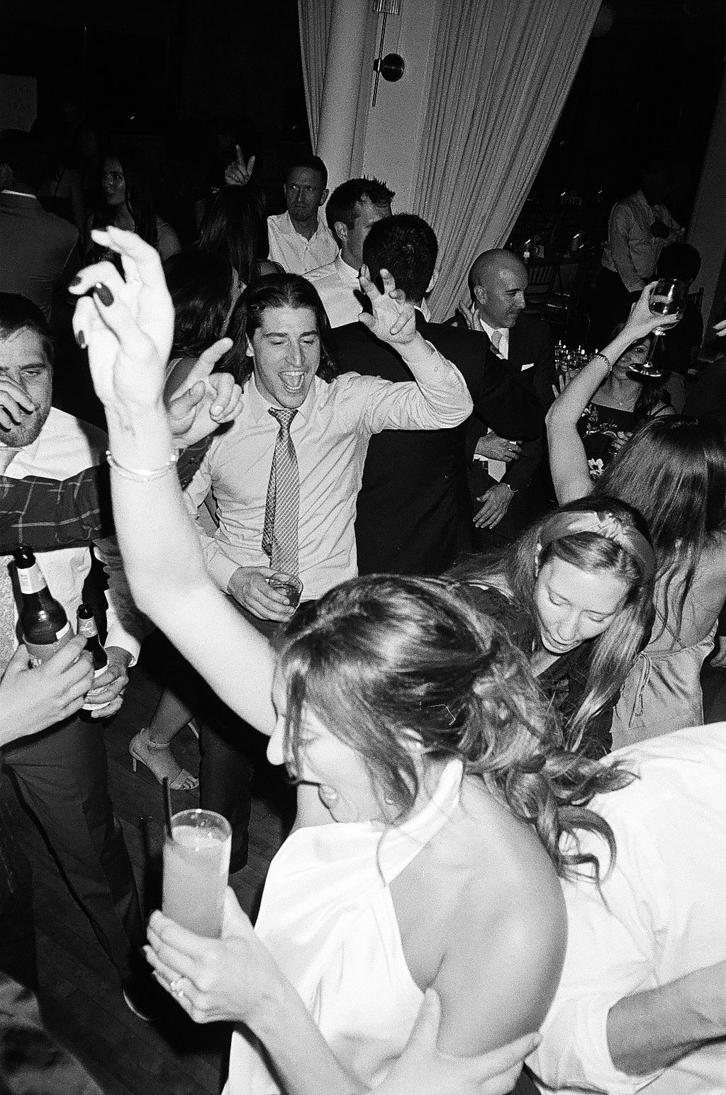 Black and white photo of guests dancing and celebrating at a lively wedding reception party.