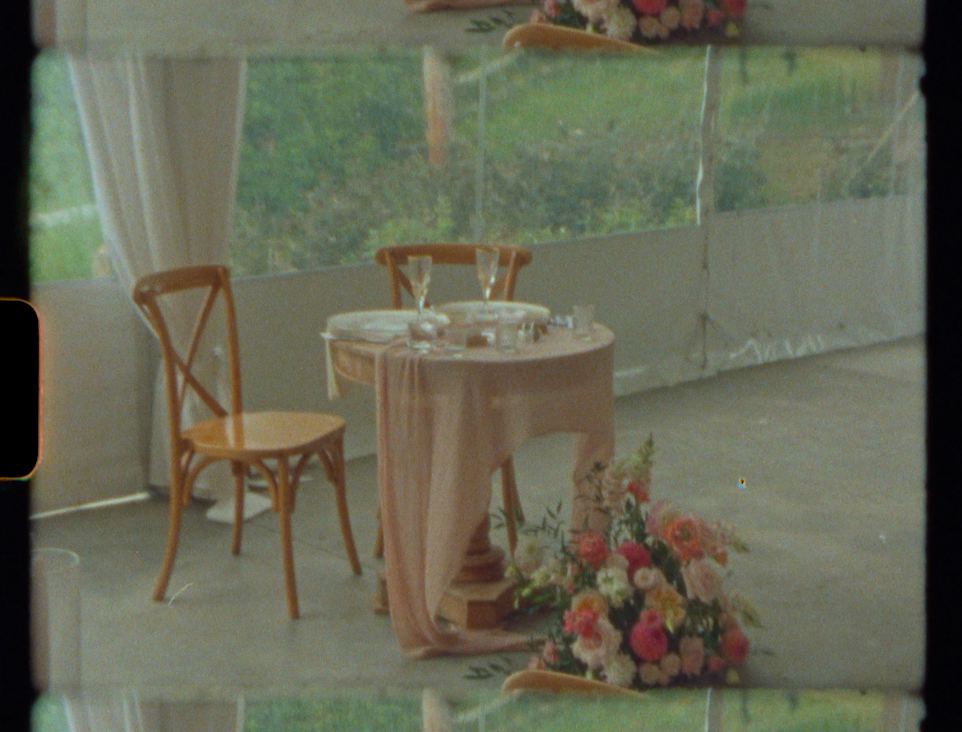 Elegant wedding sweetheart table with blush draping, wooden chairs, and colorful floral arrangements in a tent venue.