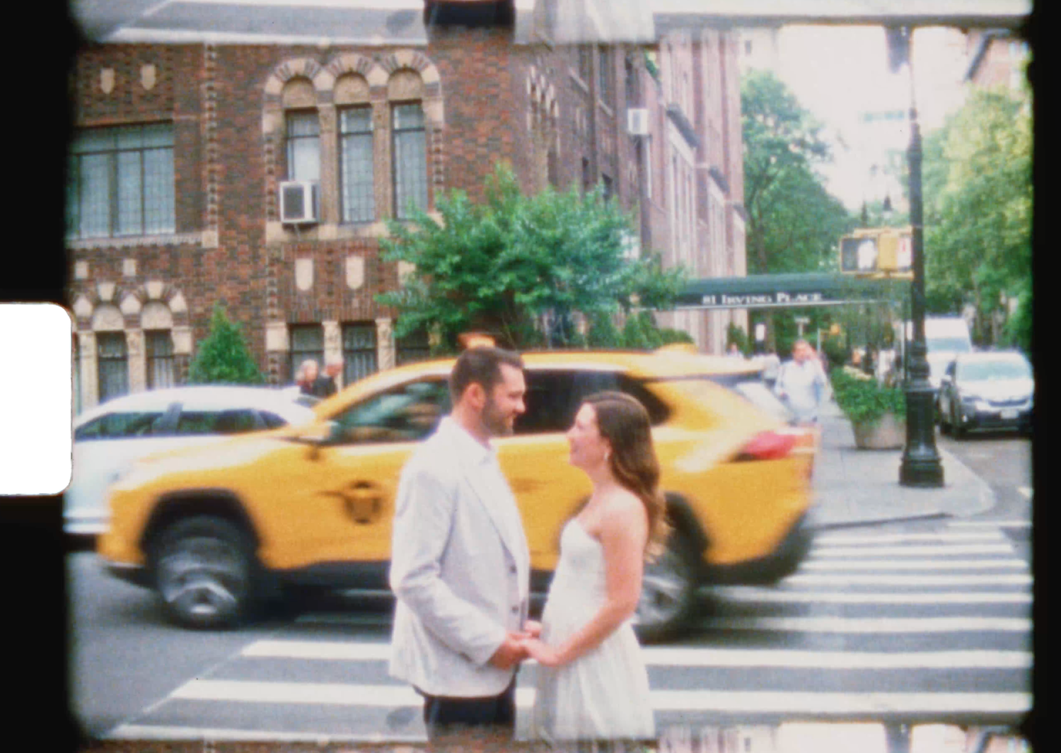 Couple holding hands at NYC crosswalk with yellow taxi cab passing behind them on a sunny day.