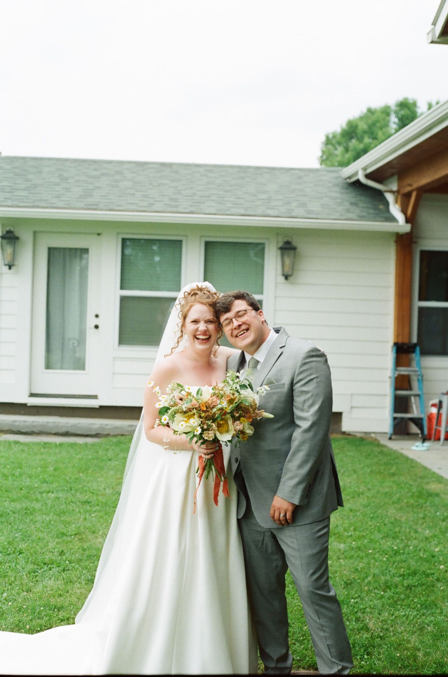 Happy bride and groom posing together outdoors on their wedding day, bride holding a bouquet.